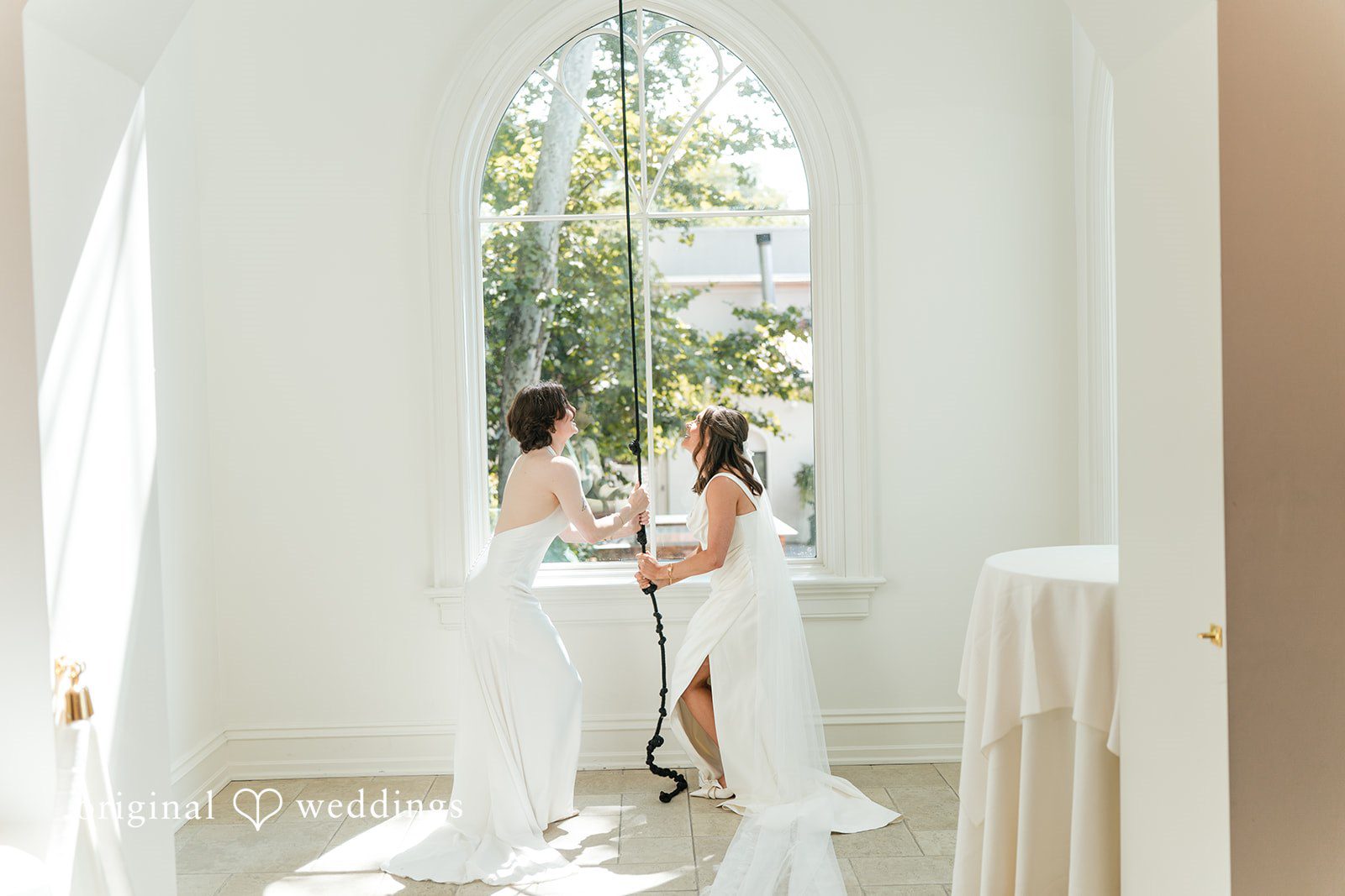 A couple standing close together and talking near a brightly lit window.
