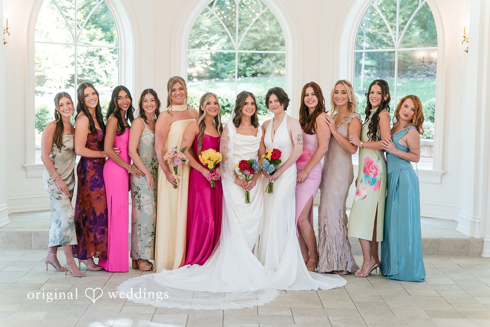 A large wedding party in colorful dresses posing together with a bride in a long veil.