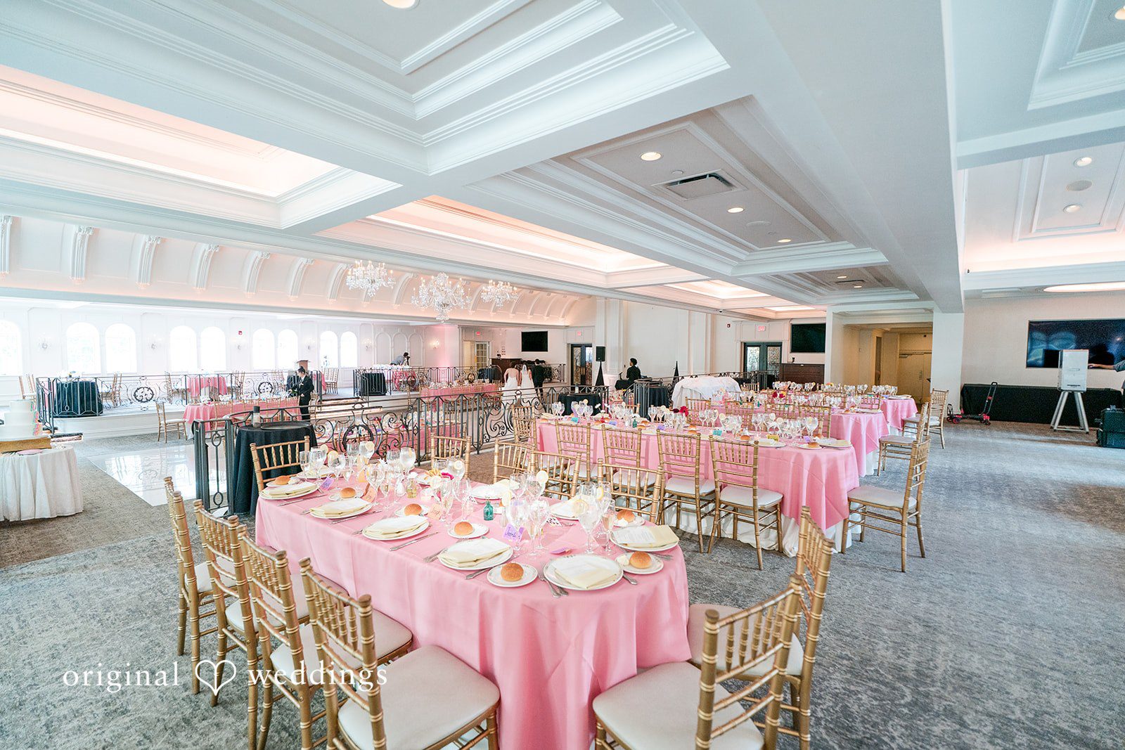 Elegant round tables with pink tablecloths set up for a reception in a large dining room.