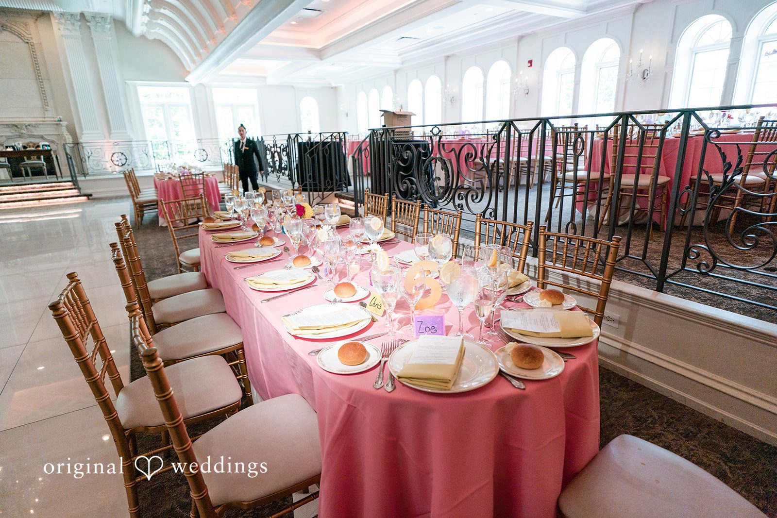 A long banquet table decorated with a pink table runner and glassware for an event.