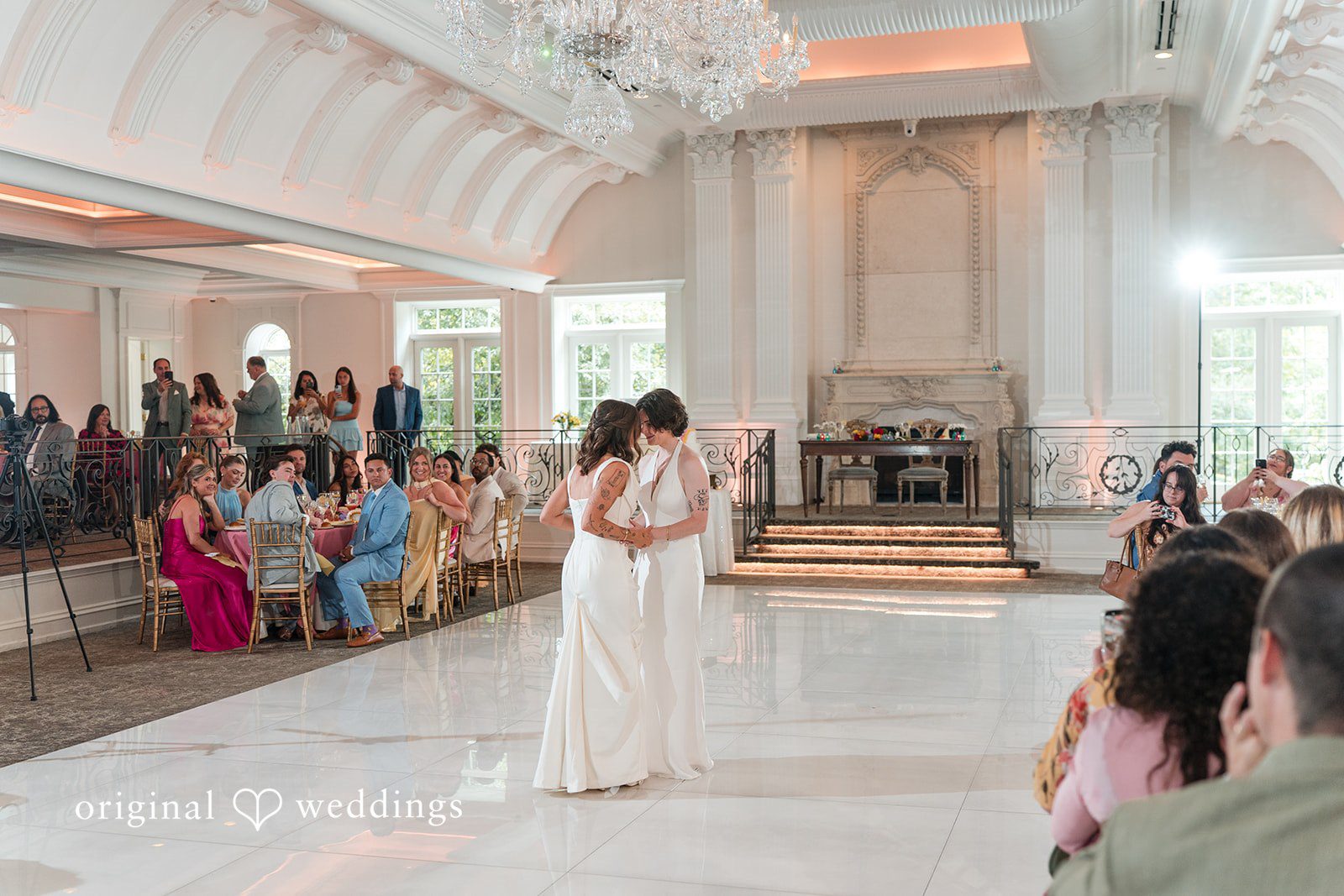 A couple dancing in the middle of a spacious reception hall surrounded by seated guests.