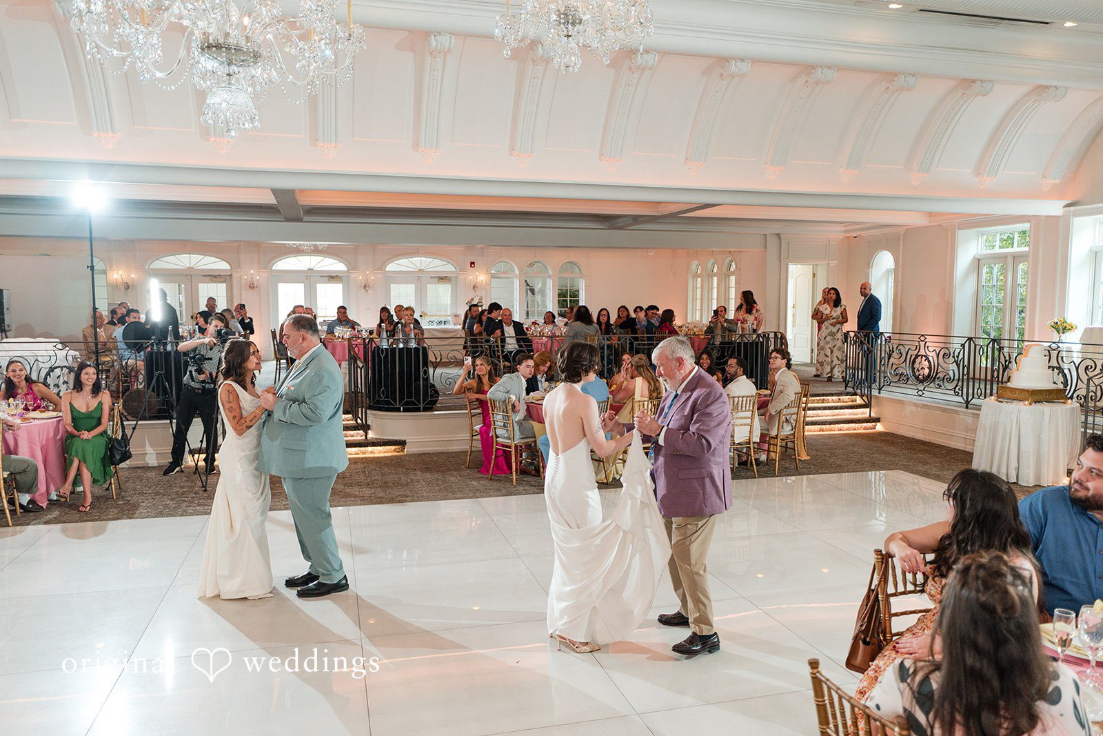Wedding guests dancing and mingling together on a brightly lit dance floor during a reception.