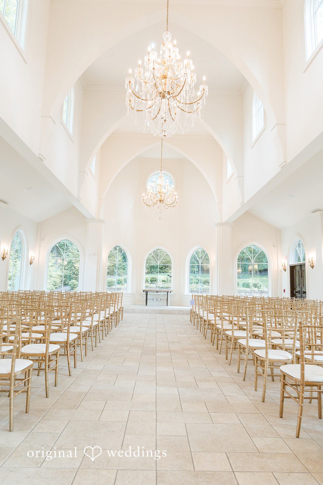 Rows of empty wooden chairs set up for a wedding ceremony inside a bright hall.