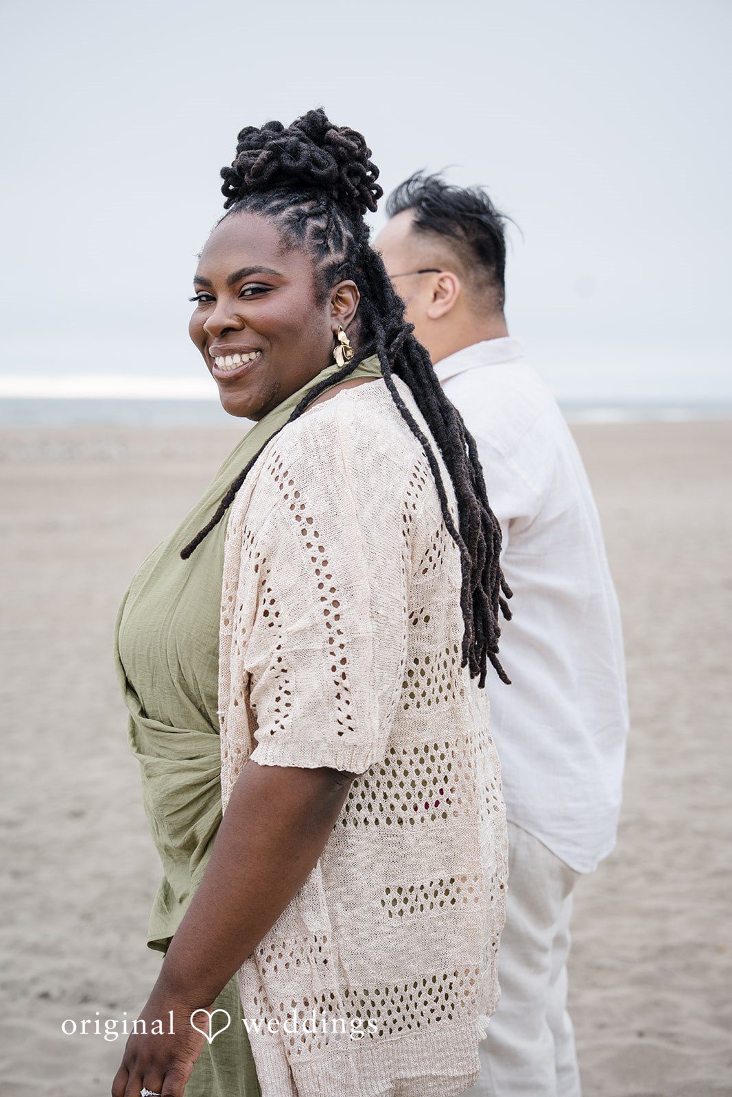 Ashley + Willard A person in an olive outfit looks over their shoulder while standing next to someone in white on the shore.