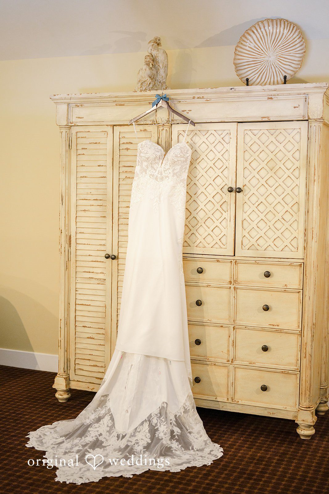 Daniel + Karen A white lace wedding dress hanging from a rustic wooden wardrobe closet.