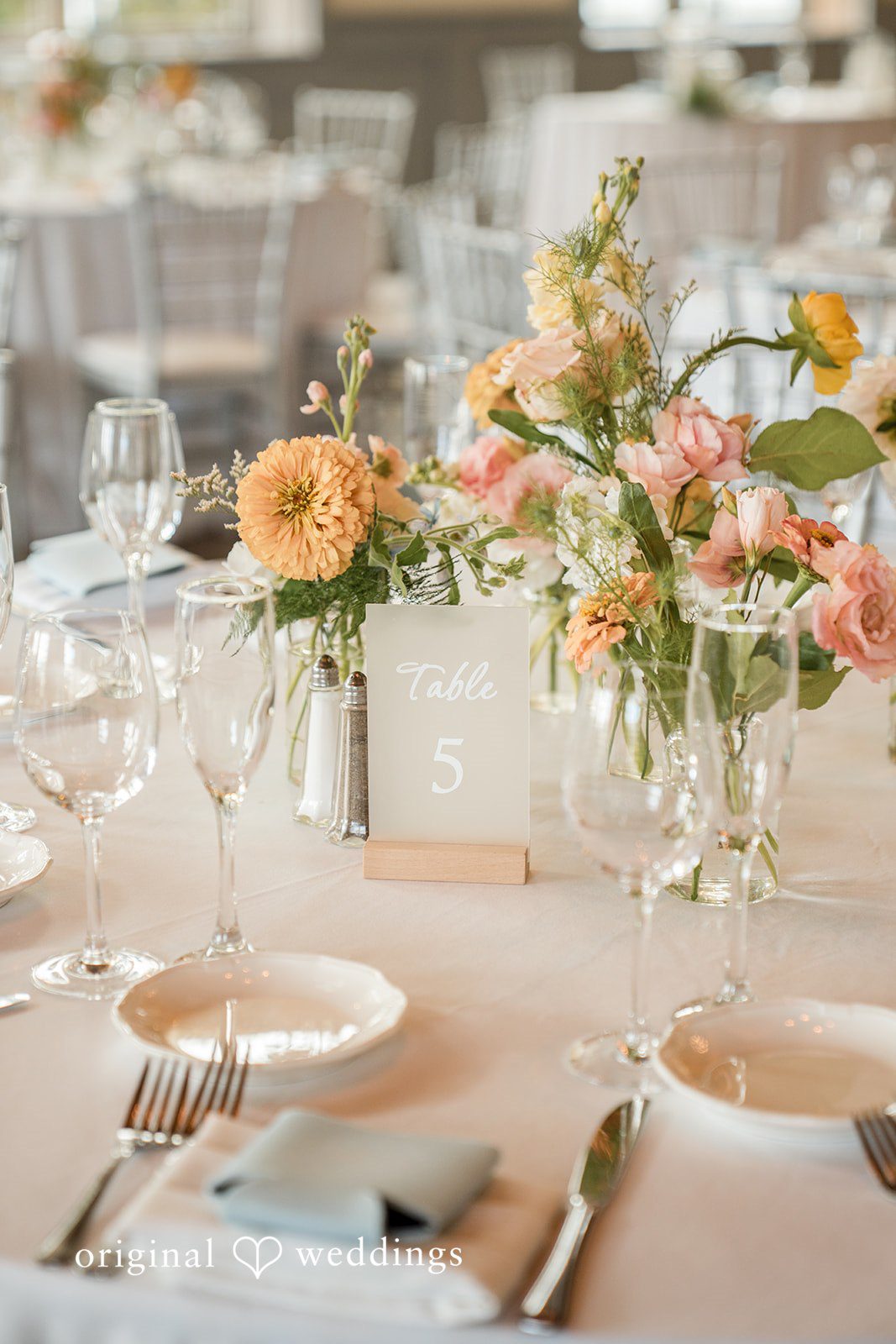 Daniel + Karen A close-up of a reception table featuring peach floral centerpieces and formal place settings.