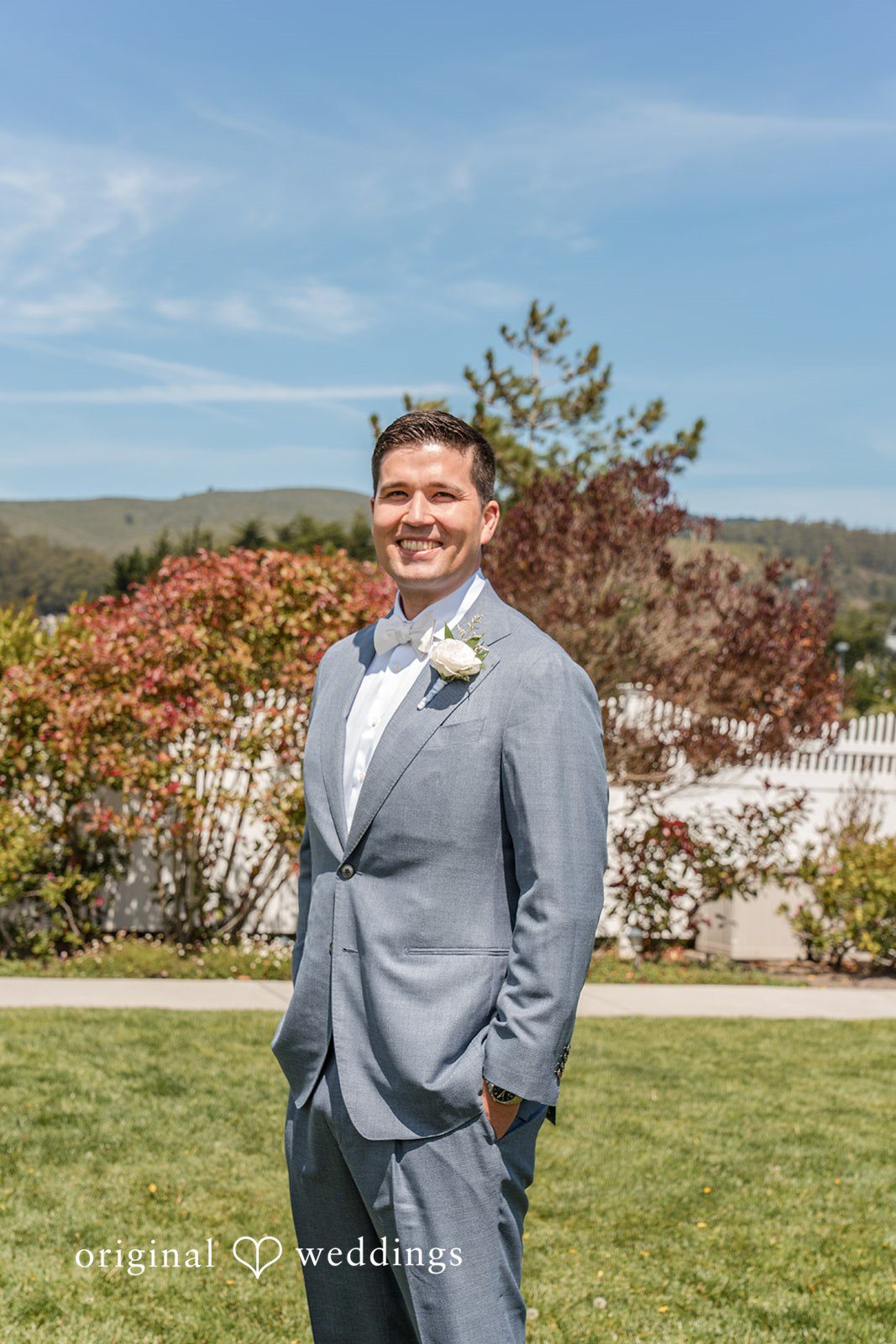 Daniel + Karen A groom posing solo in a textured light grey suit against a scenic nature backdrop.