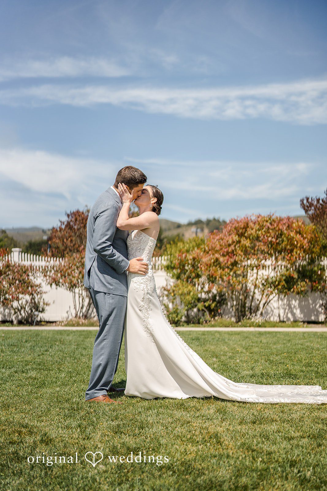 Daniel + Karen A bride and groom kissing on a grassy hill overlooking a scenic coastline.