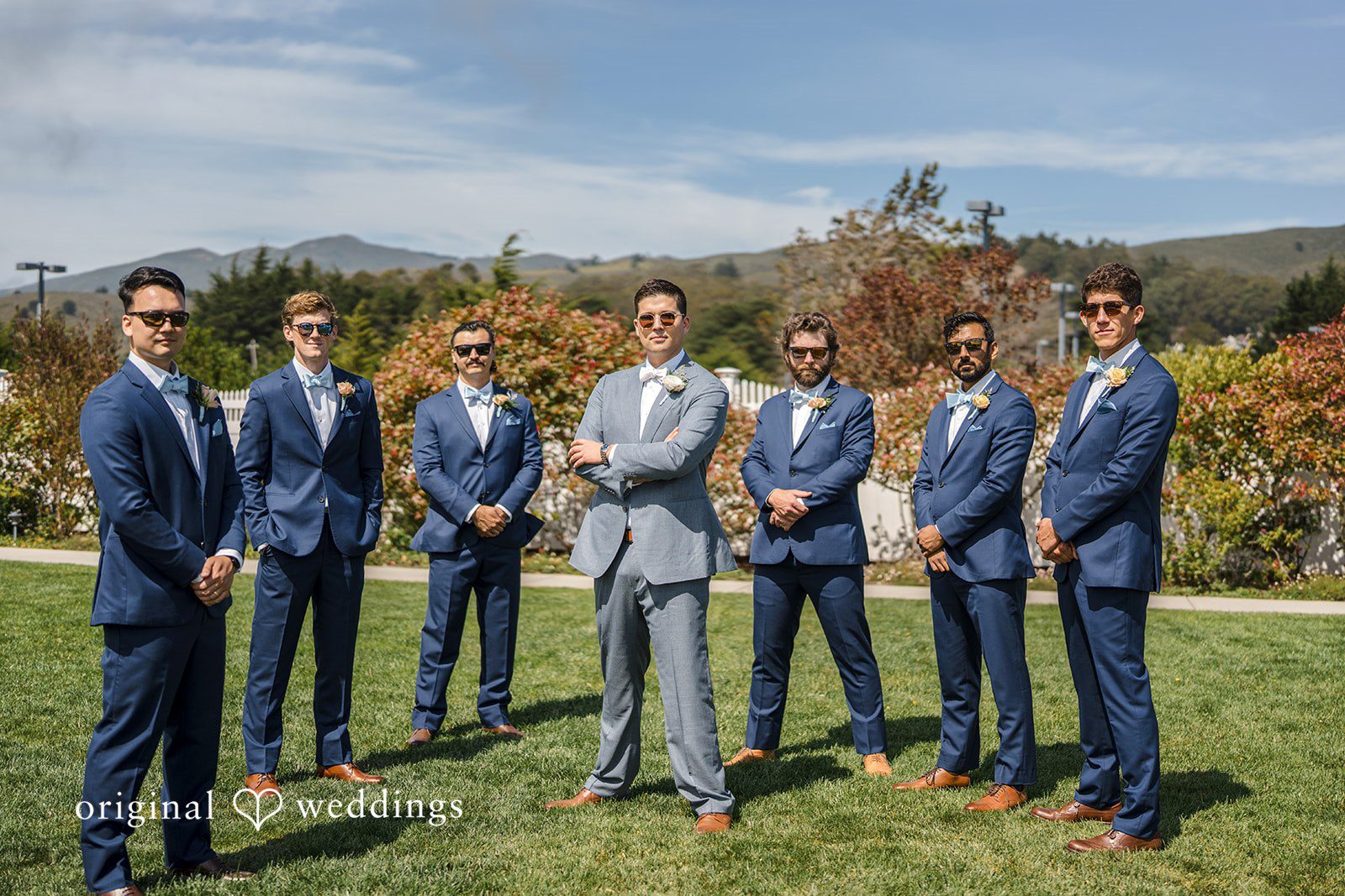Daniel + Karen A groom and his groomsmen standing together in matching blue suits on a grassy hill.