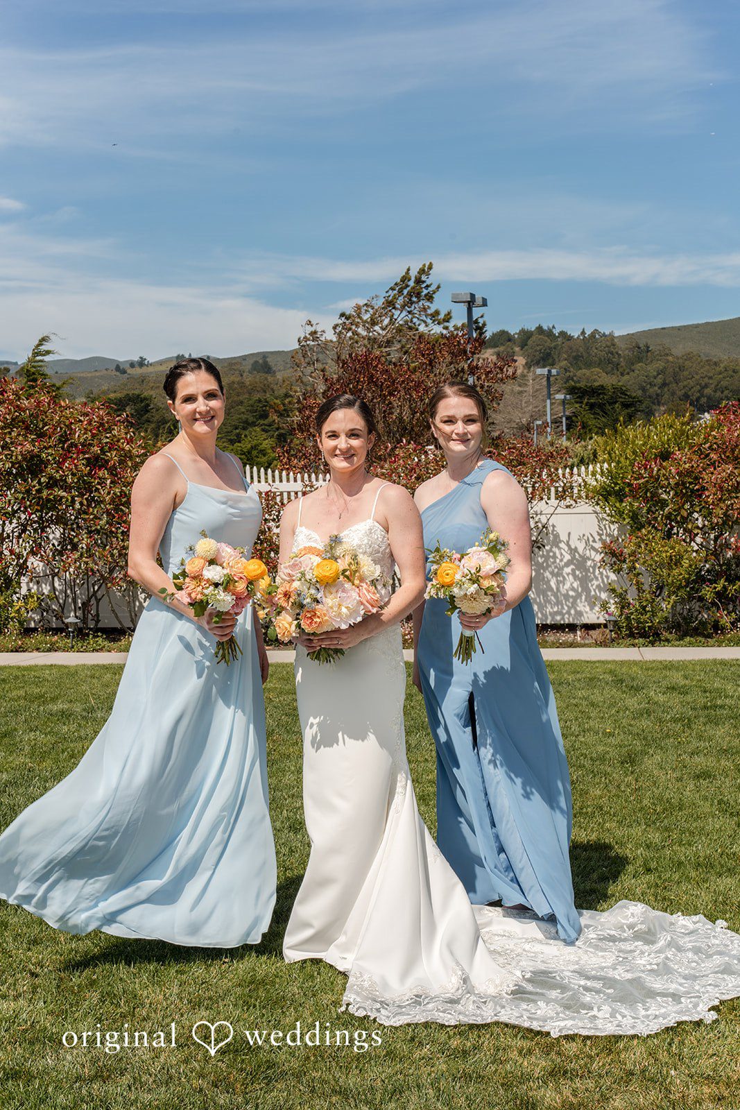 Daniel + Karen A bride posing on a lawn with her bridesmaids dressed in light blue gowns.