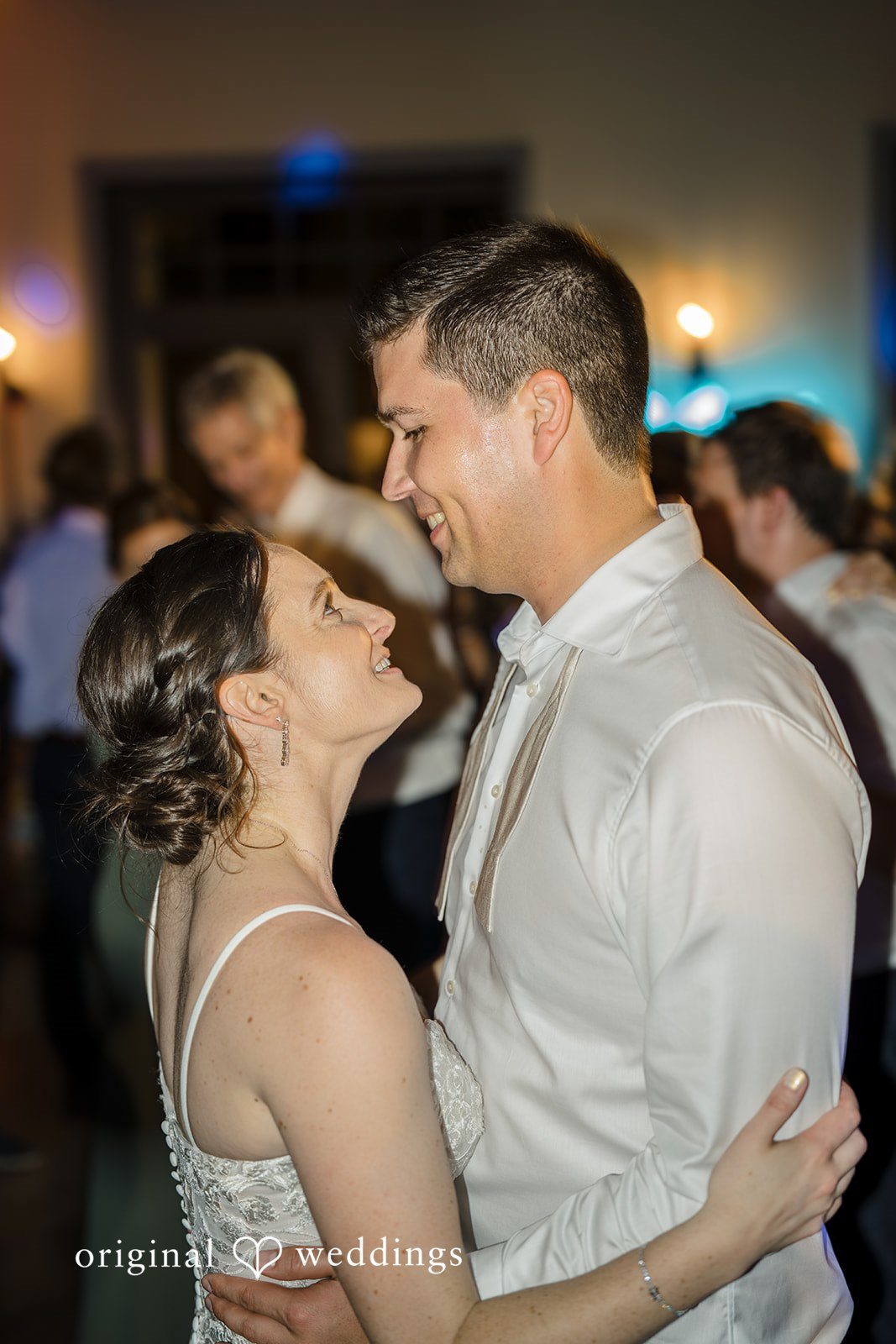 Daniel + Karen A groom smiling at his bride closely on a dimly lit dance floor.
