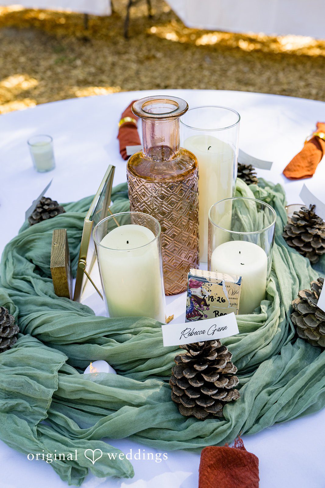 Abigail + Reece A centerpiece featuring candles, pinecones, and green fabric wrapping.