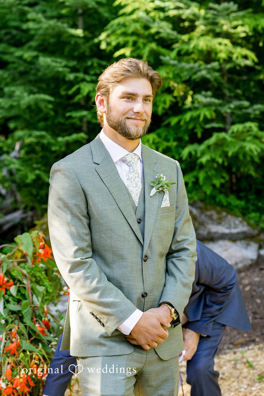 Abigail + Reece A groom in a light sage green suit smiling.