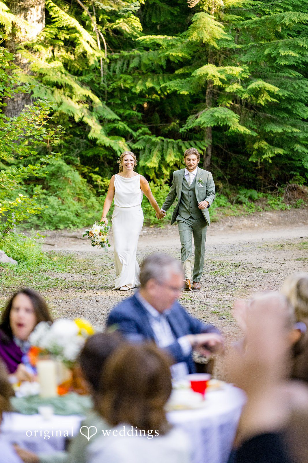 Abigail + Reece A bride and groom running along a path toward wedding guests.