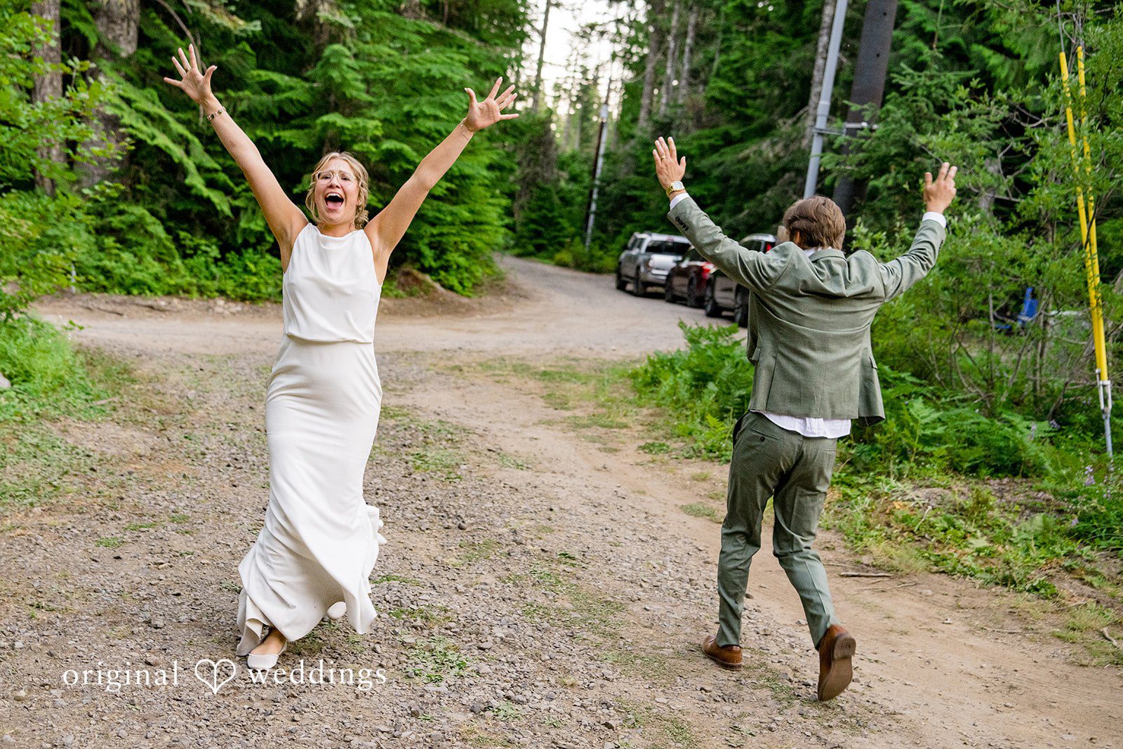 Abigail + Reece A bride and groom celebrating with raised arms on a gravel pathway.