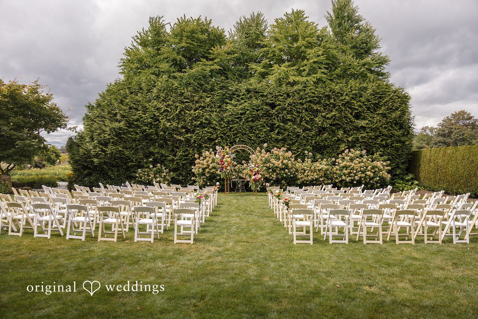 Diego + Adel An arrangement of empty white chairs set up on a grassy lawn for a ceremony.
