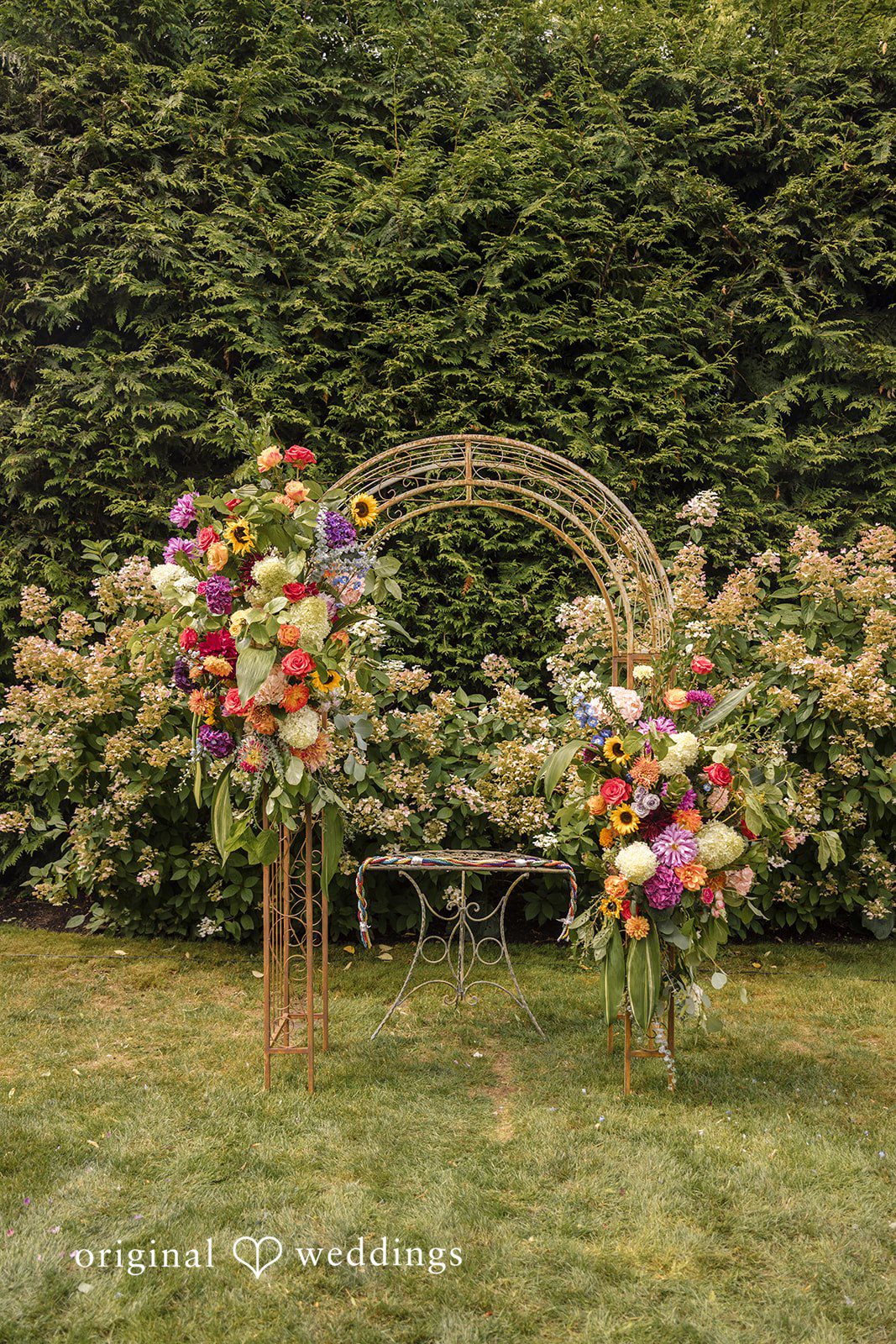 Diego + Adel A circular floral arch filled with colorful blossoms standing on a lawn.