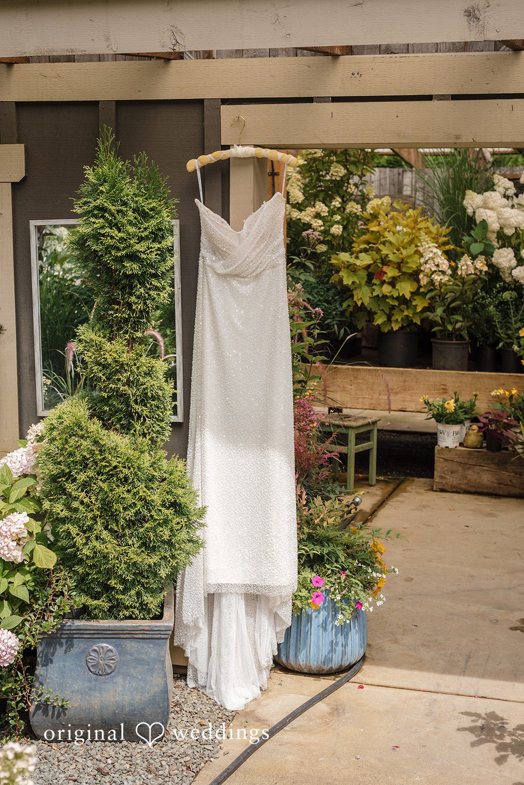 Diego + Adel A white lace wedding dress hanging up outside in a garden pathway.