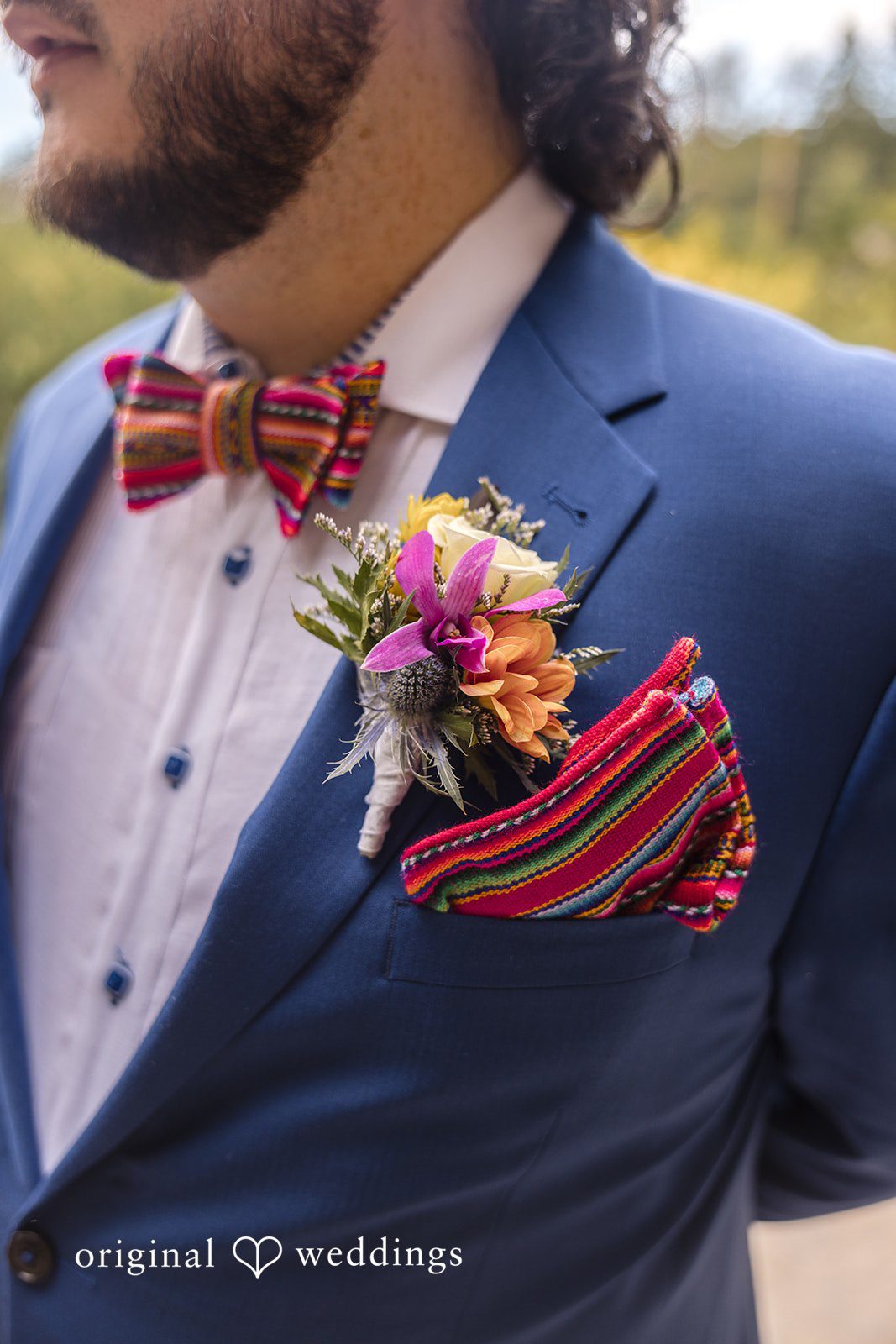 Diego + Adel A close-up portrait of a groom in a blue suit with a colorful boutonniere and matching bow tie.