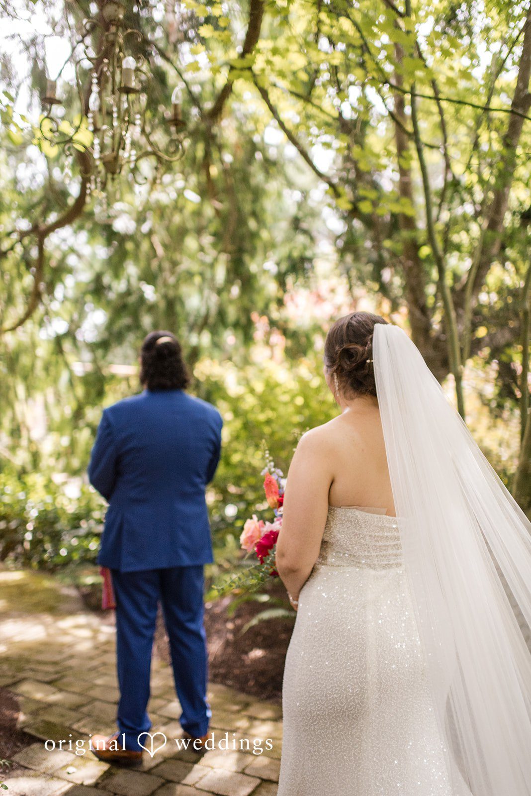 Diego + Adel A back view of a bride with a long veil walking alongside her groom.