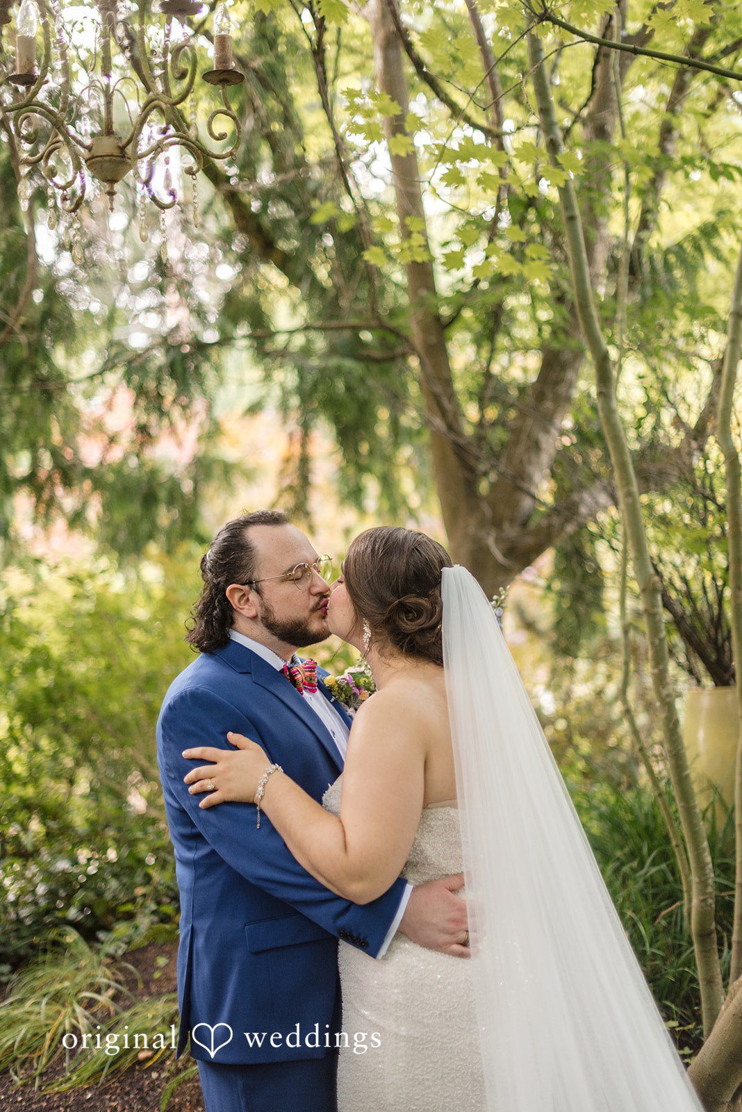Diego + Adel A groom embracing his bride from behind in a sunlit garden.
