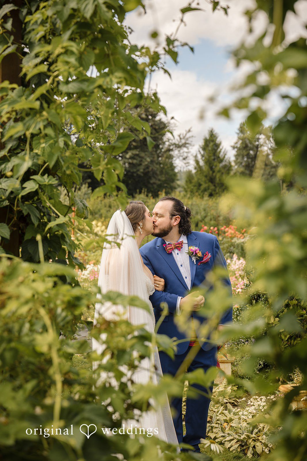 Diego + Adel A bride and groom sharing a close embrace among tall green pine trees.