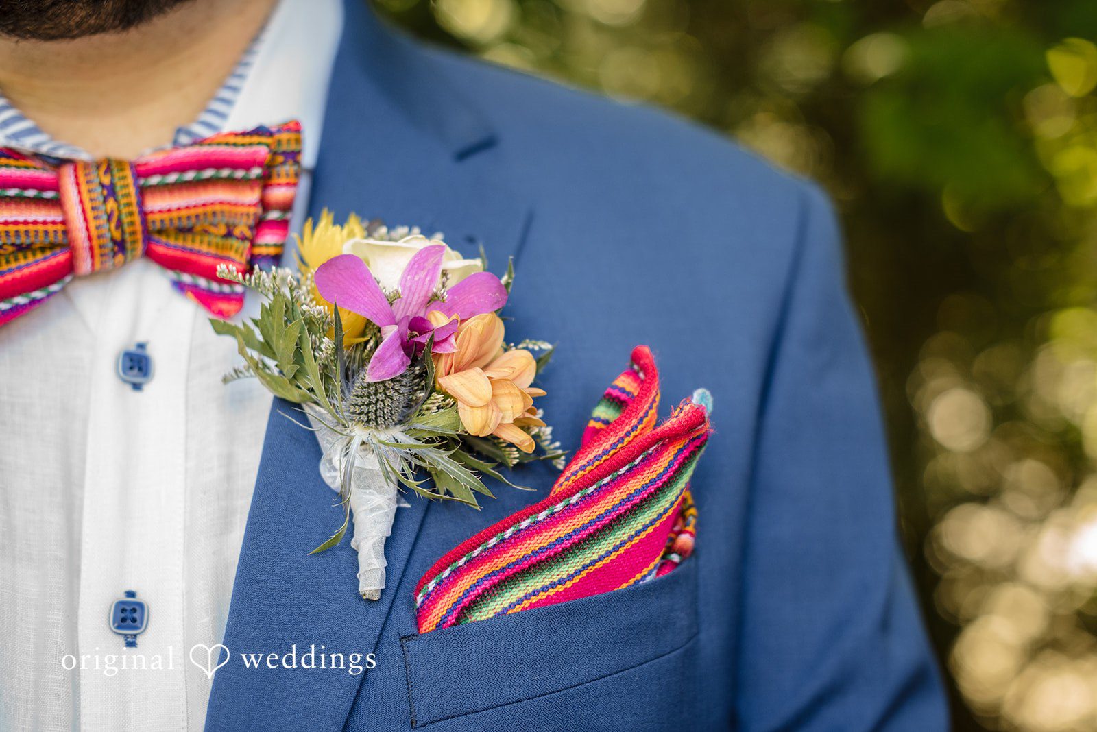 Diego + Adel A close-up of a blue suit jacket pocket adorned with a colorful floral boutonniere and a patterned pocket square.