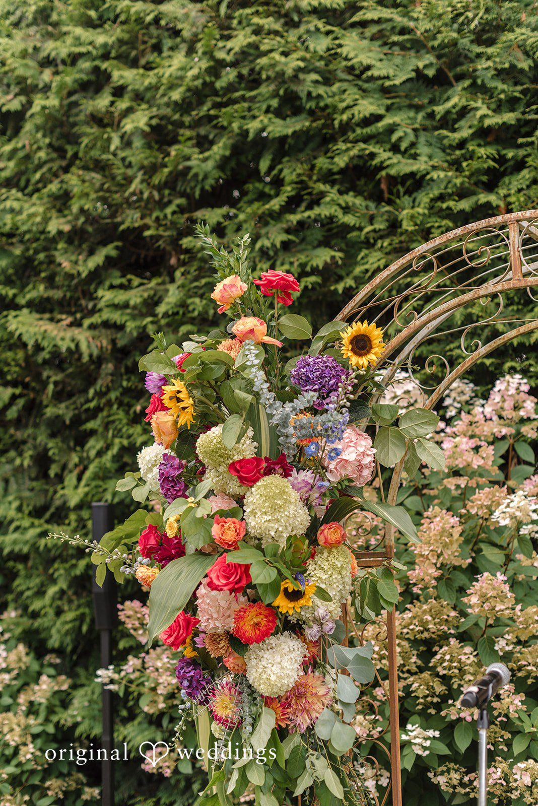 Diego + Adel A close-up view of a vibrant wedding arch heavily decorated with multi-colored flowers.