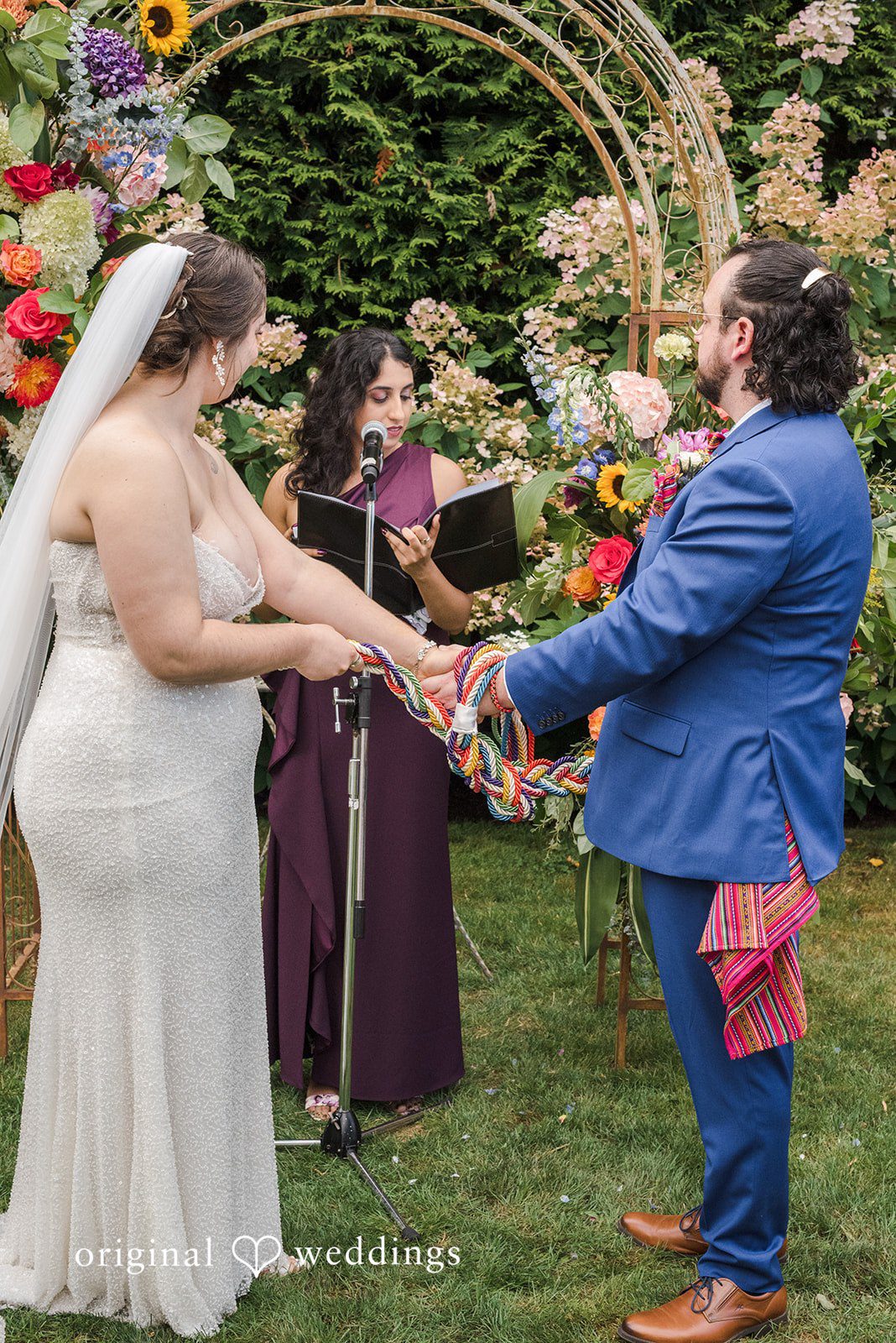 Diego + Adel A bride and groom exchanging vows under a colorful floral arch.