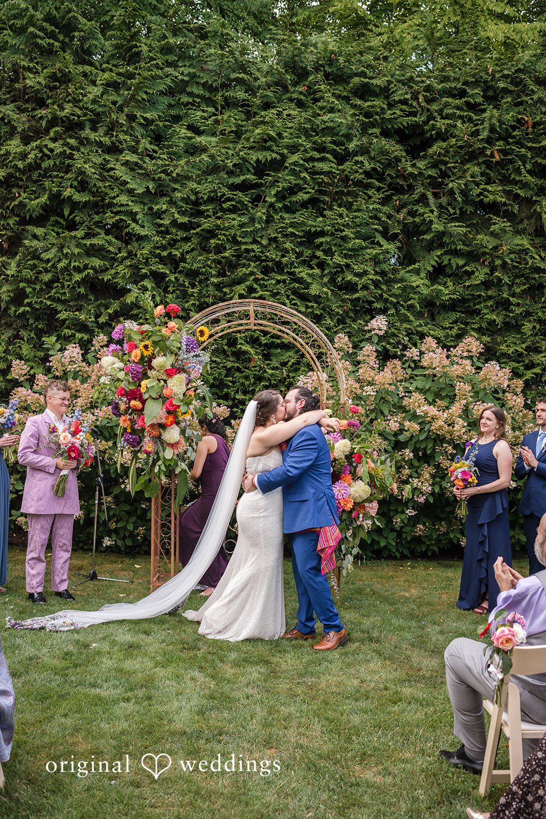 Diego + Adel A bride and groom sharing a kiss at the altar in front of a green hedge.