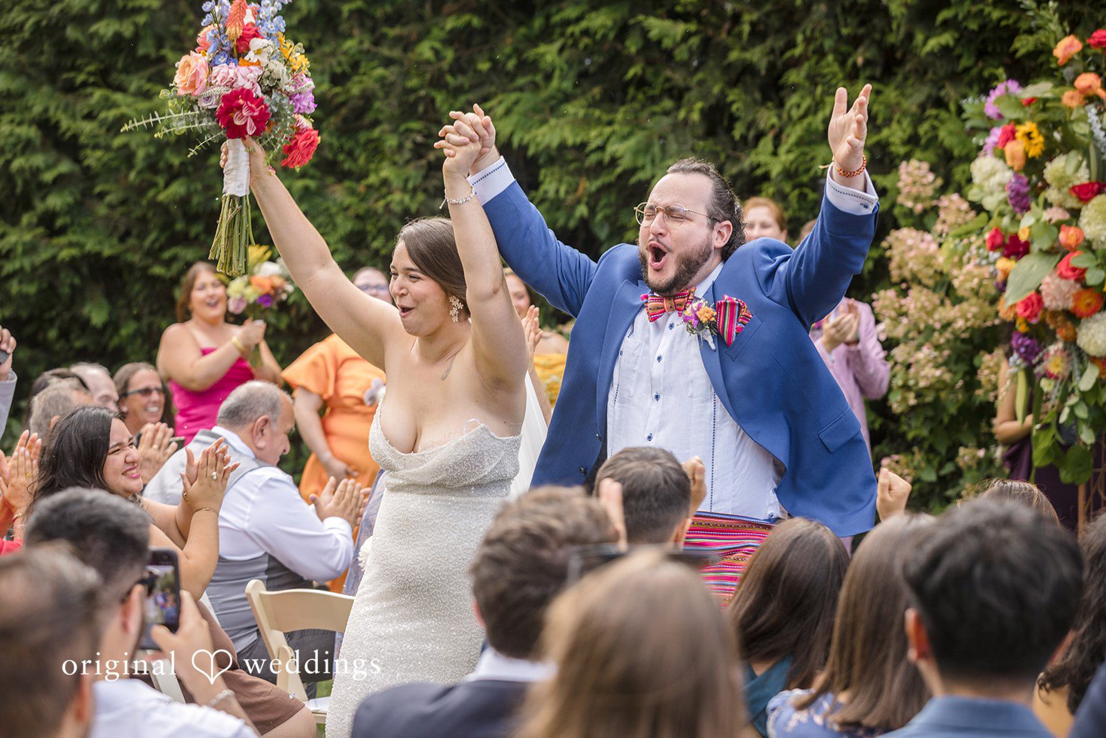 Diego + Adel A newly married couple cheering with their arms raised as they walk down the aisle.