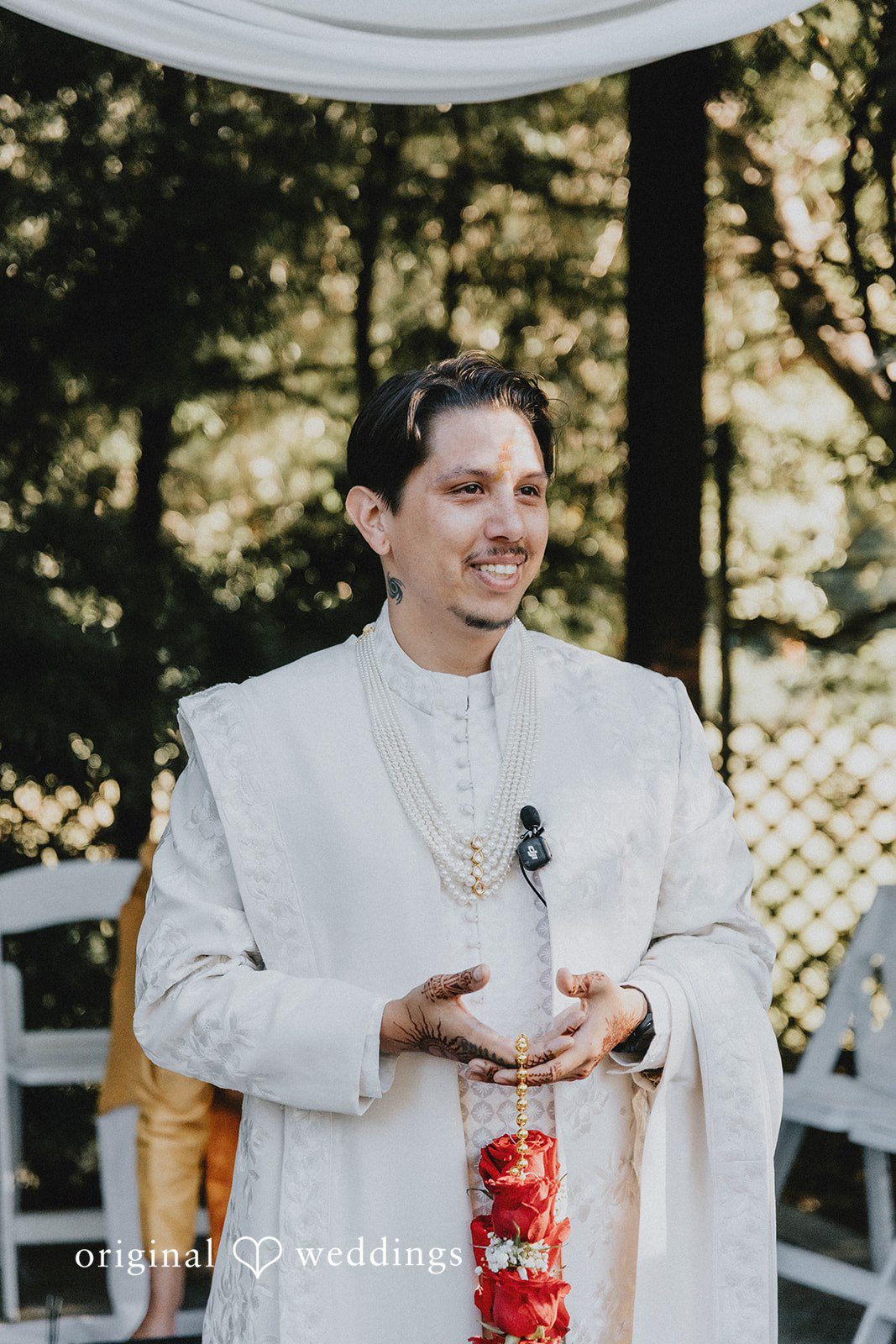 A groom in a white sherwani smiling during a wedding ritual.