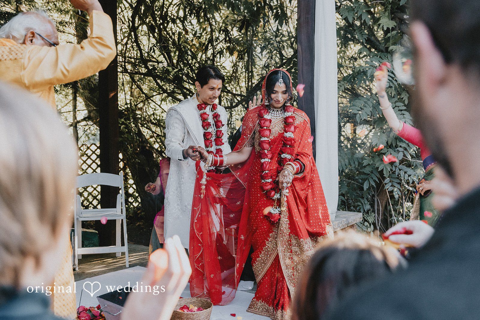 A bride and groom walking together through a wooded area.