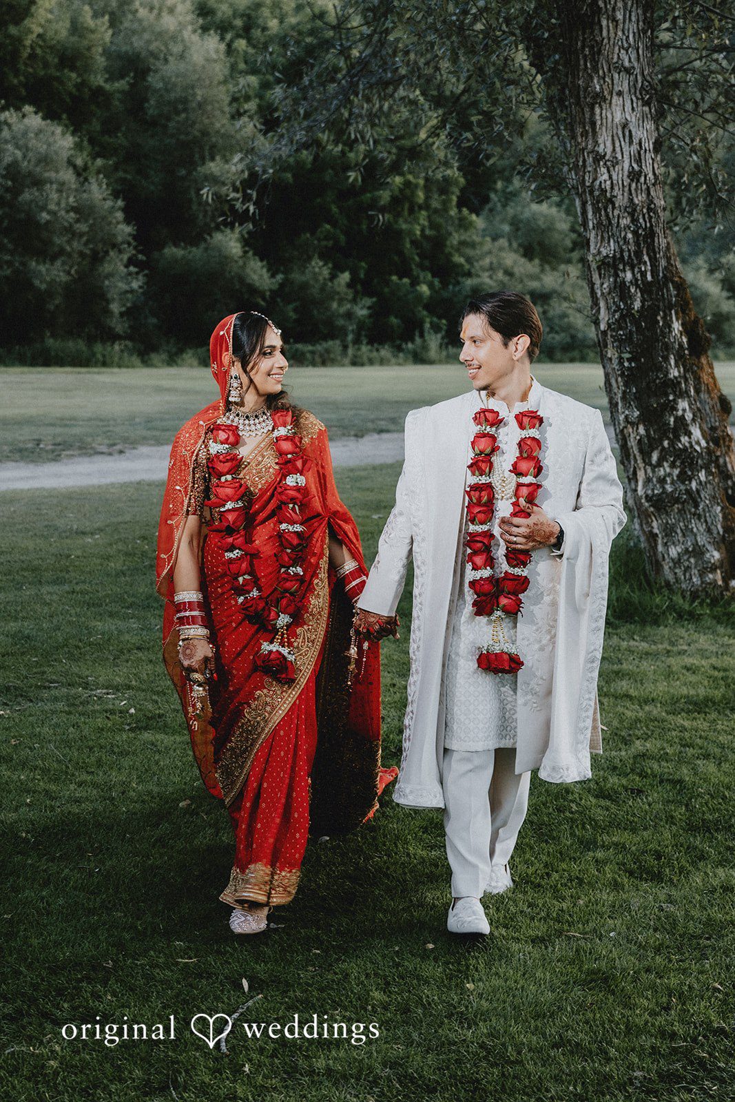A bride and groom walking side by side across a green lawn.