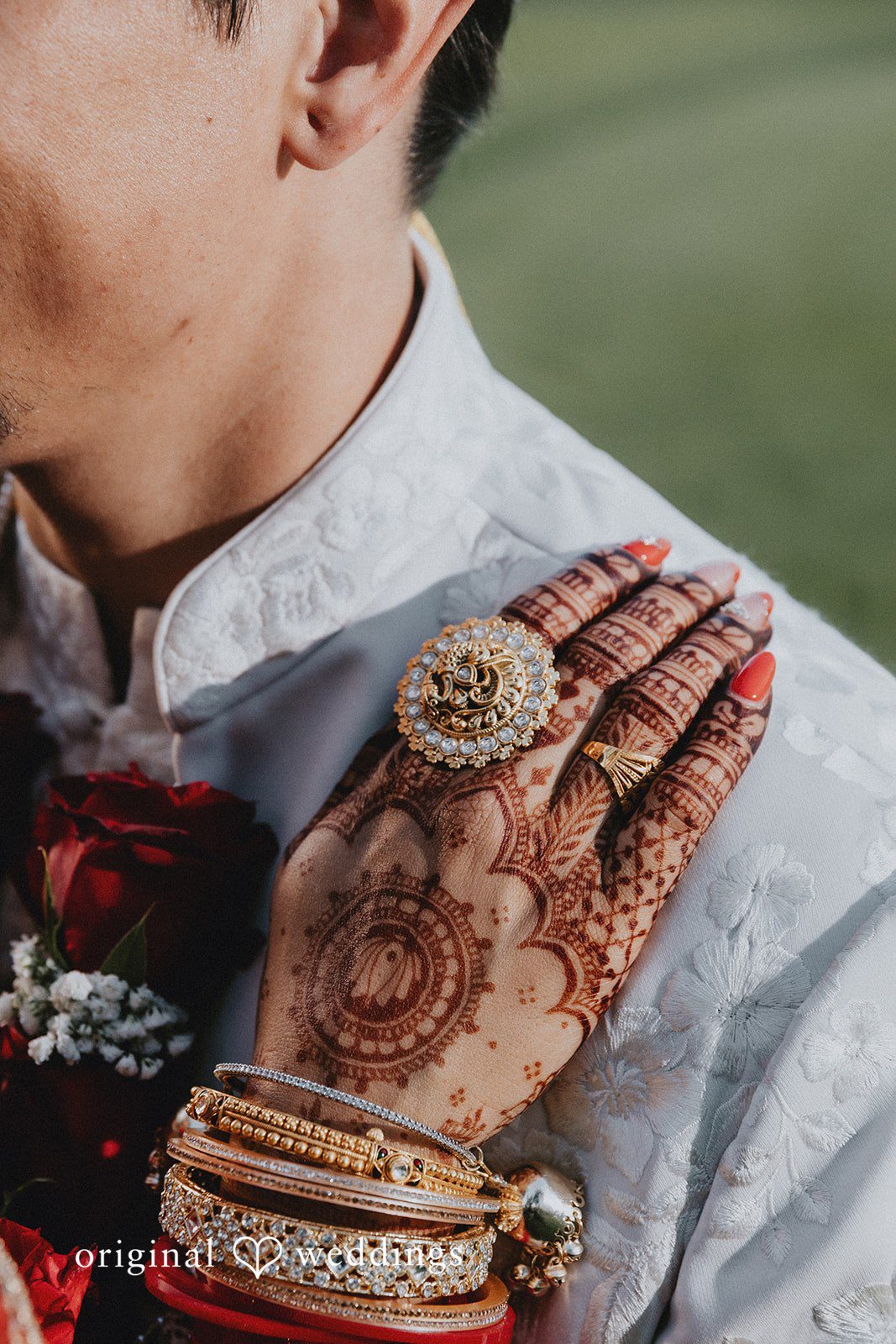 A close-up view of a hand decorated with detailed henna resting on a groom's shoulder.