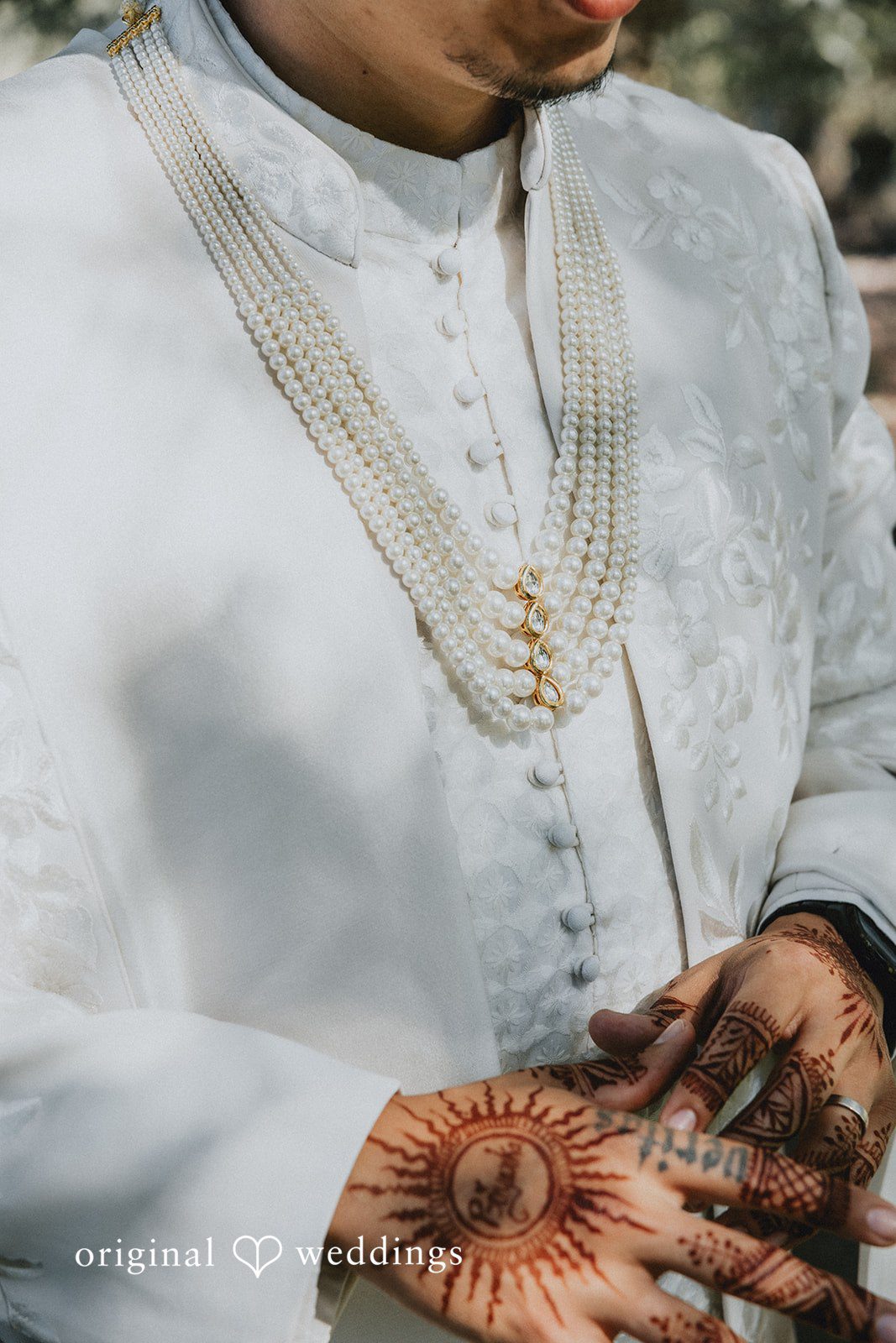 A close-up view of a groom wearing a textured white sherwani.