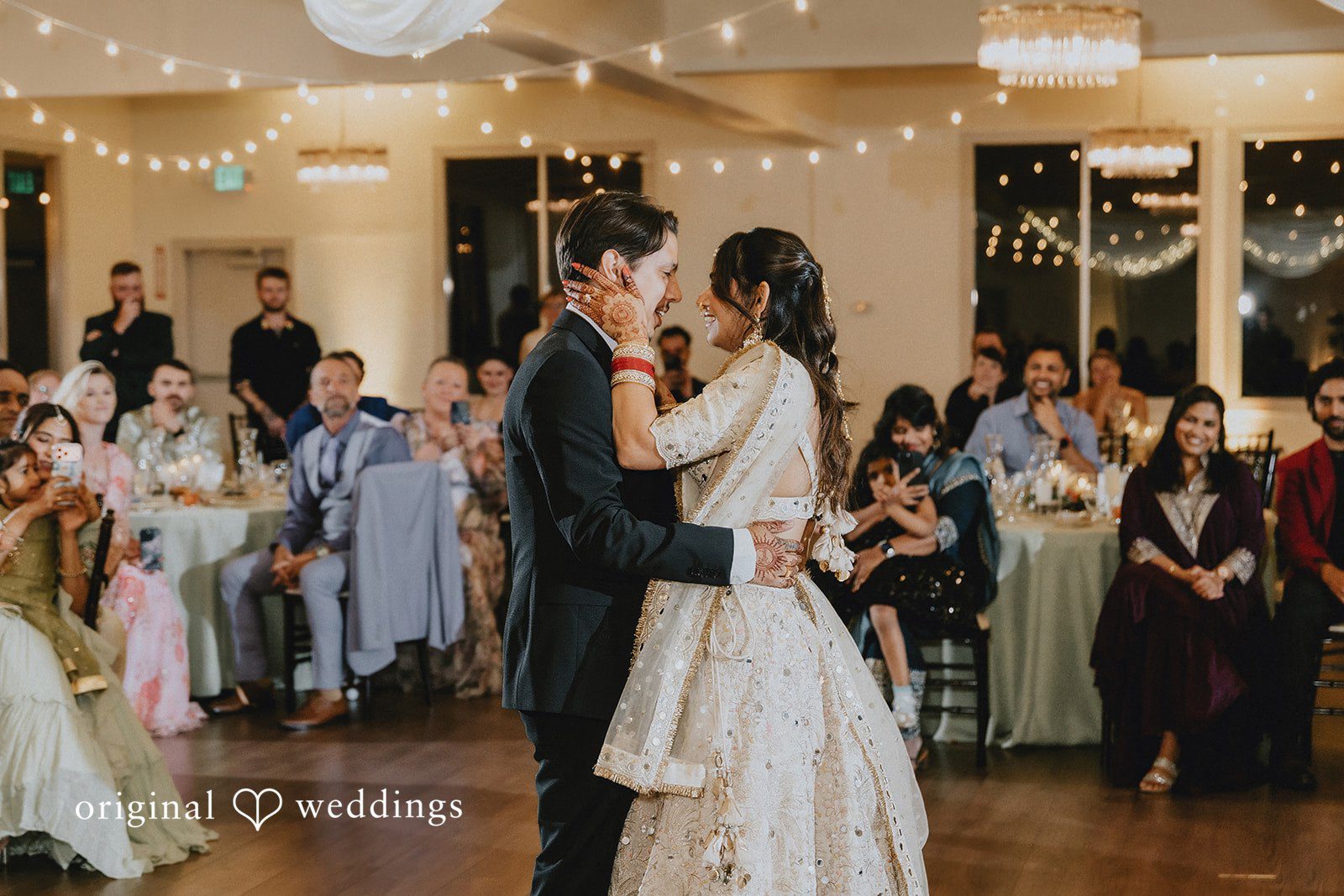 A bride and groom dancing together in the center of a crowded ballroom reception.