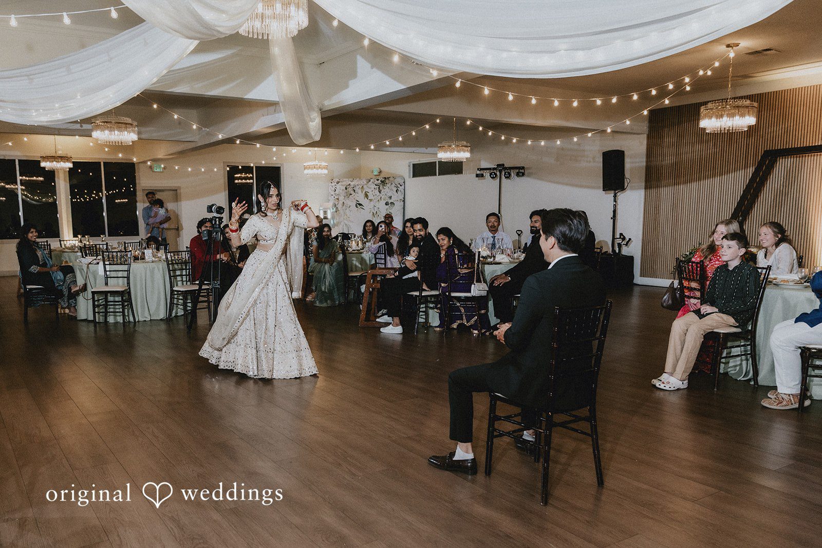 A bride dancing on a wooden dance floor while guests watch from their seats.