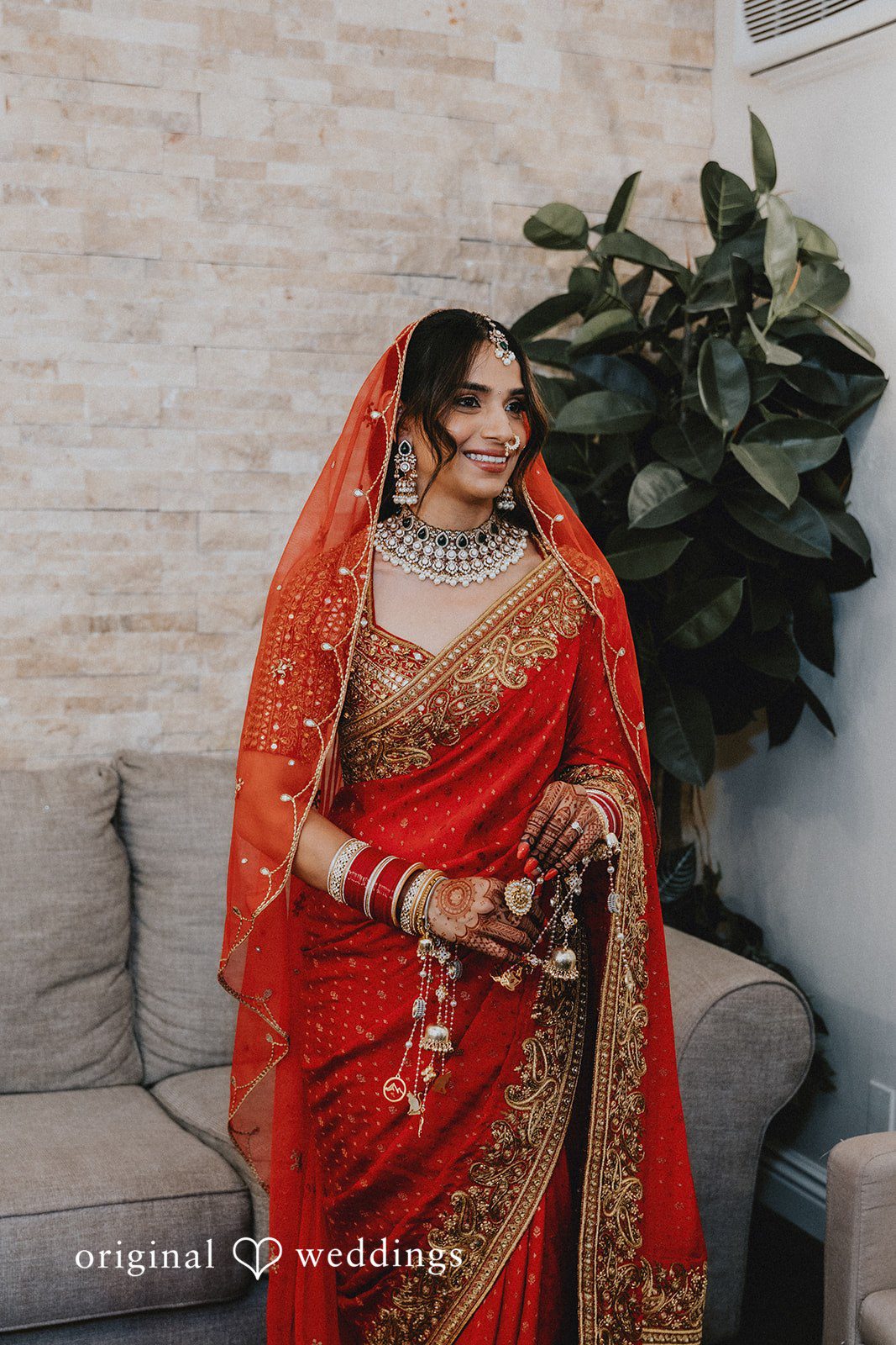 A bride posing in a traditional embroidered red lehenga with a veil.