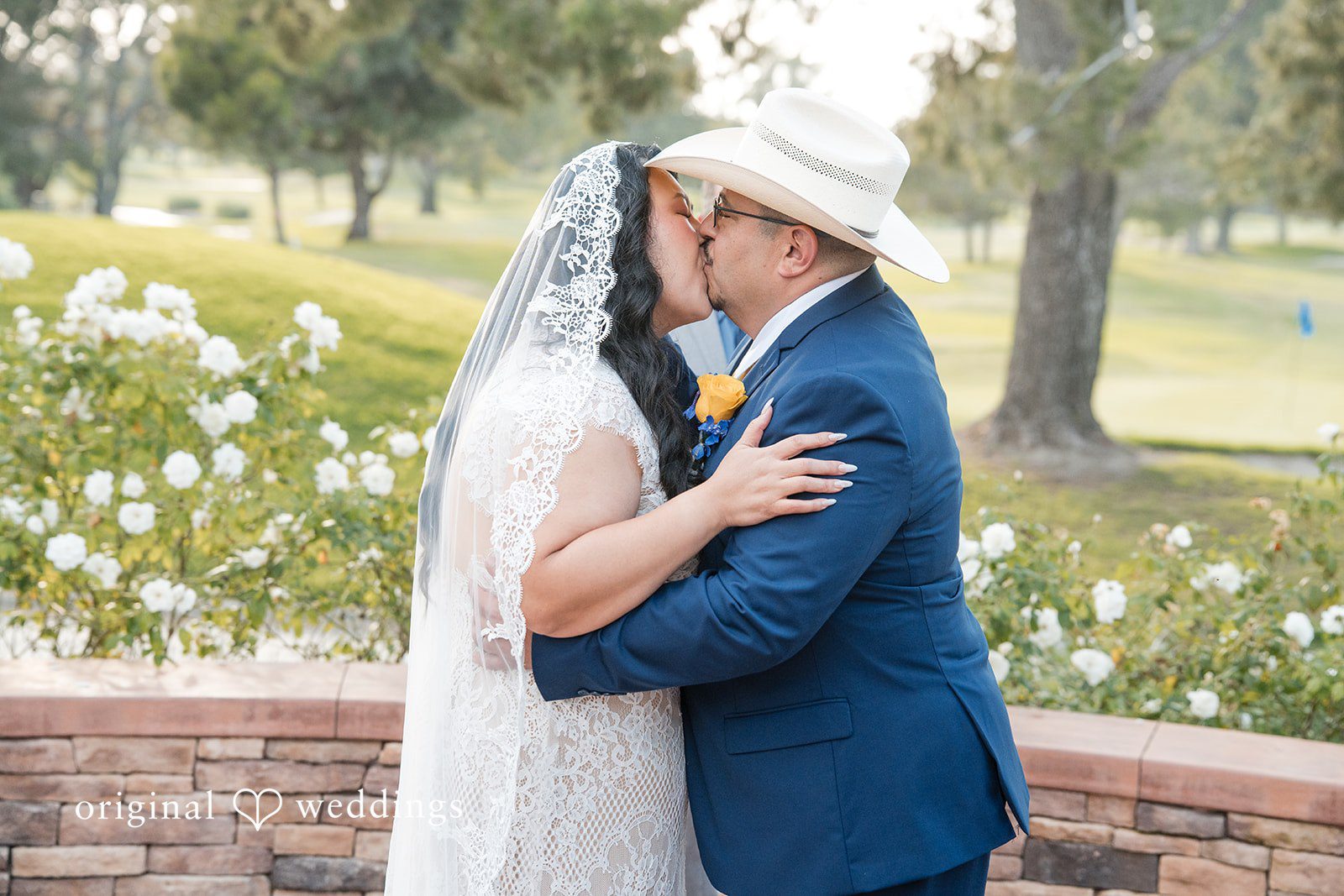 A groom embracing his bride tightly under a sunny sky.