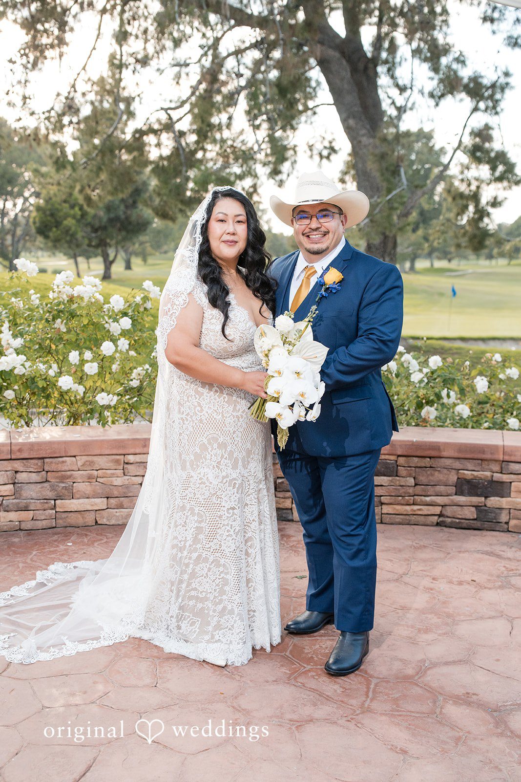 A bride and groom posing together while holding a white bouquet.