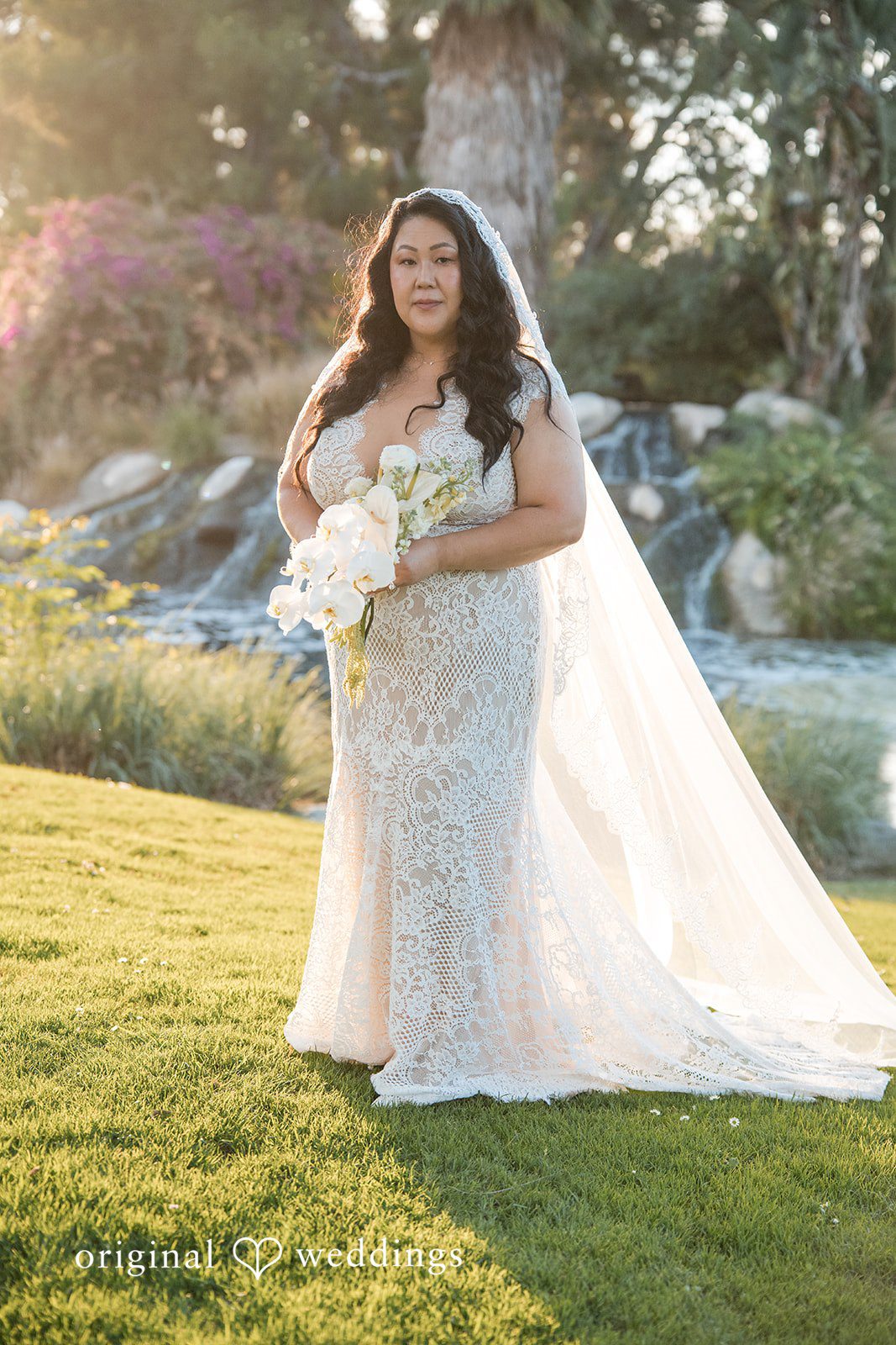 A bride in a white gown posing on a green lawn.