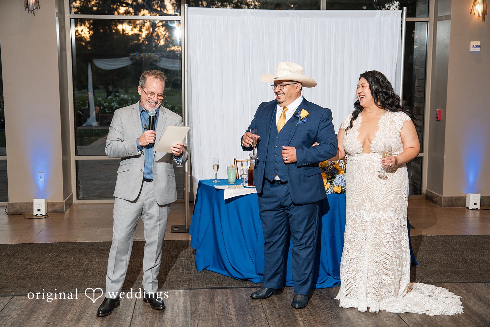 A speaker standing at a microphone next to the newlyweds at the reception.