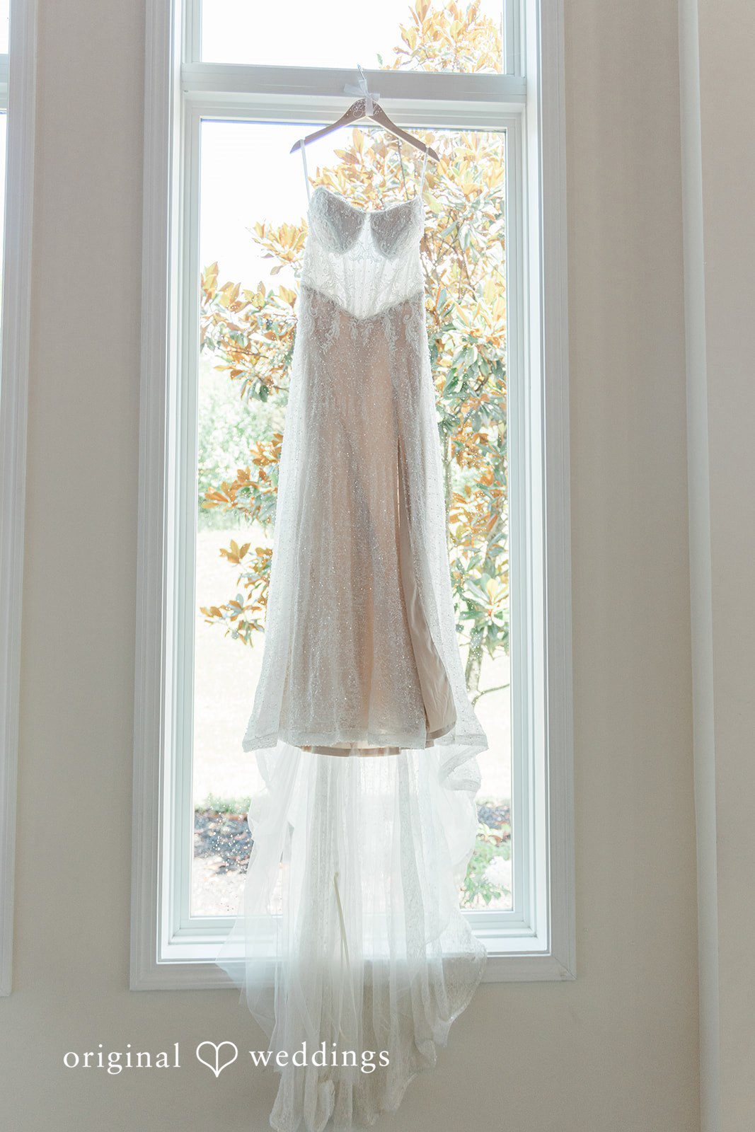 Alexander + Annalisse A white wedding dress hangs gracefully inside a tall, arched window frame.