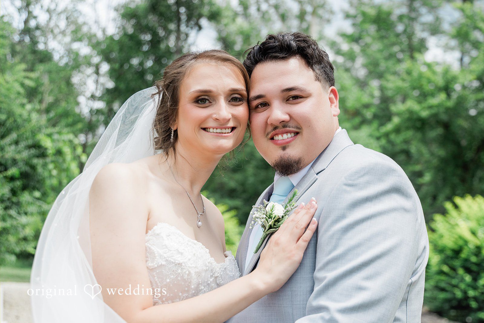 Alexander + Annalisse A bride with a veil smiles warmly next to a groom in a grey suit.