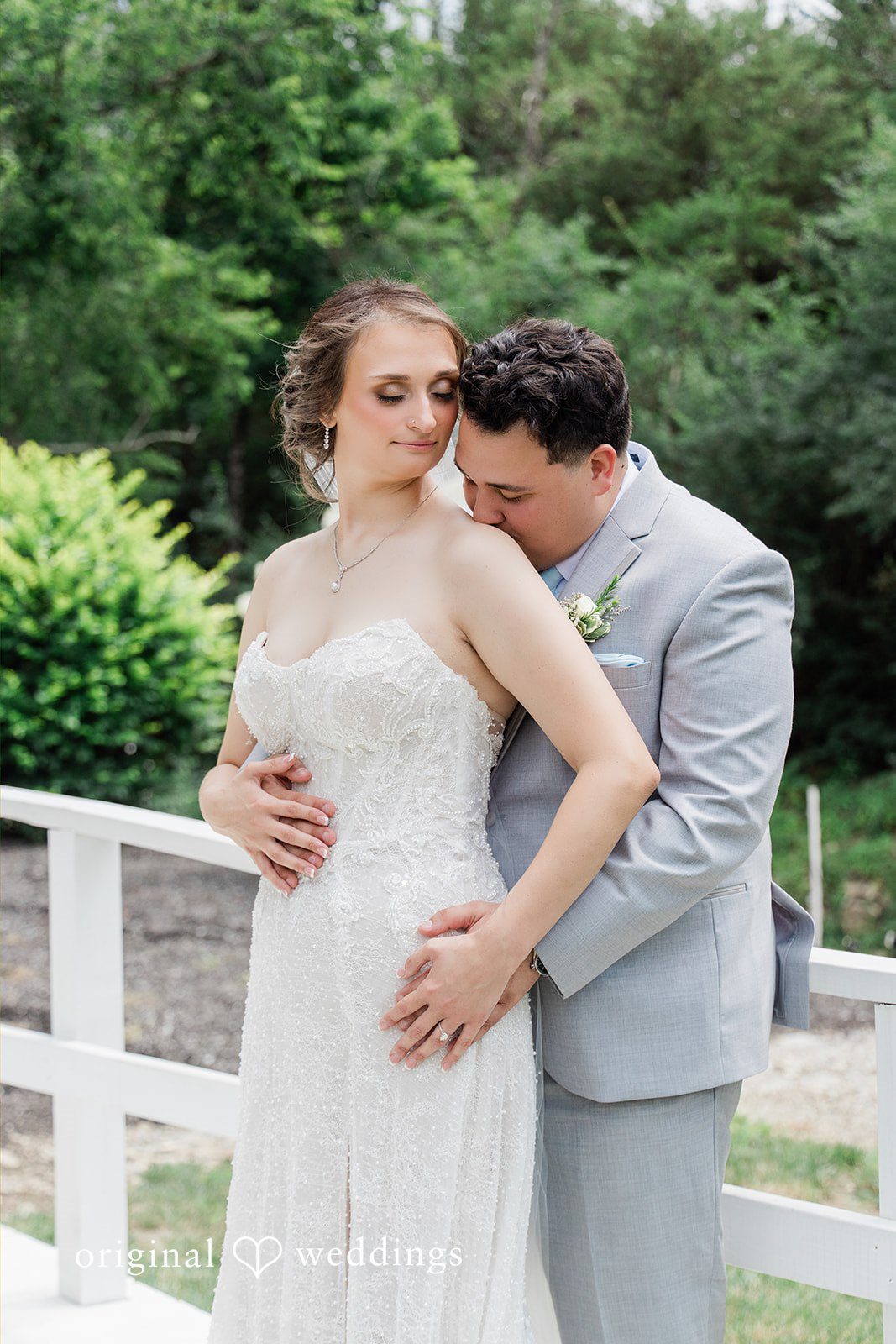 Alexander + Annalisse A groom lovingly wraps his arms around his bride's waist from behind.