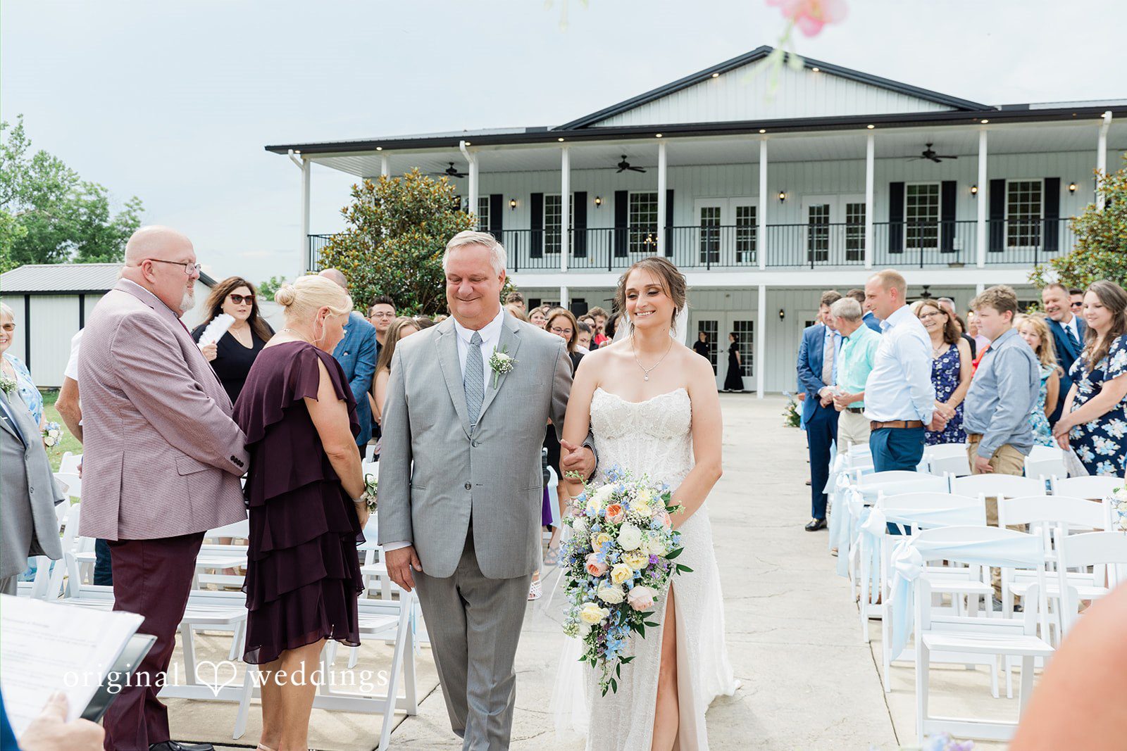 Alexander + Annalisse Wedding guests walk along a path near a large reception tent or venue building.