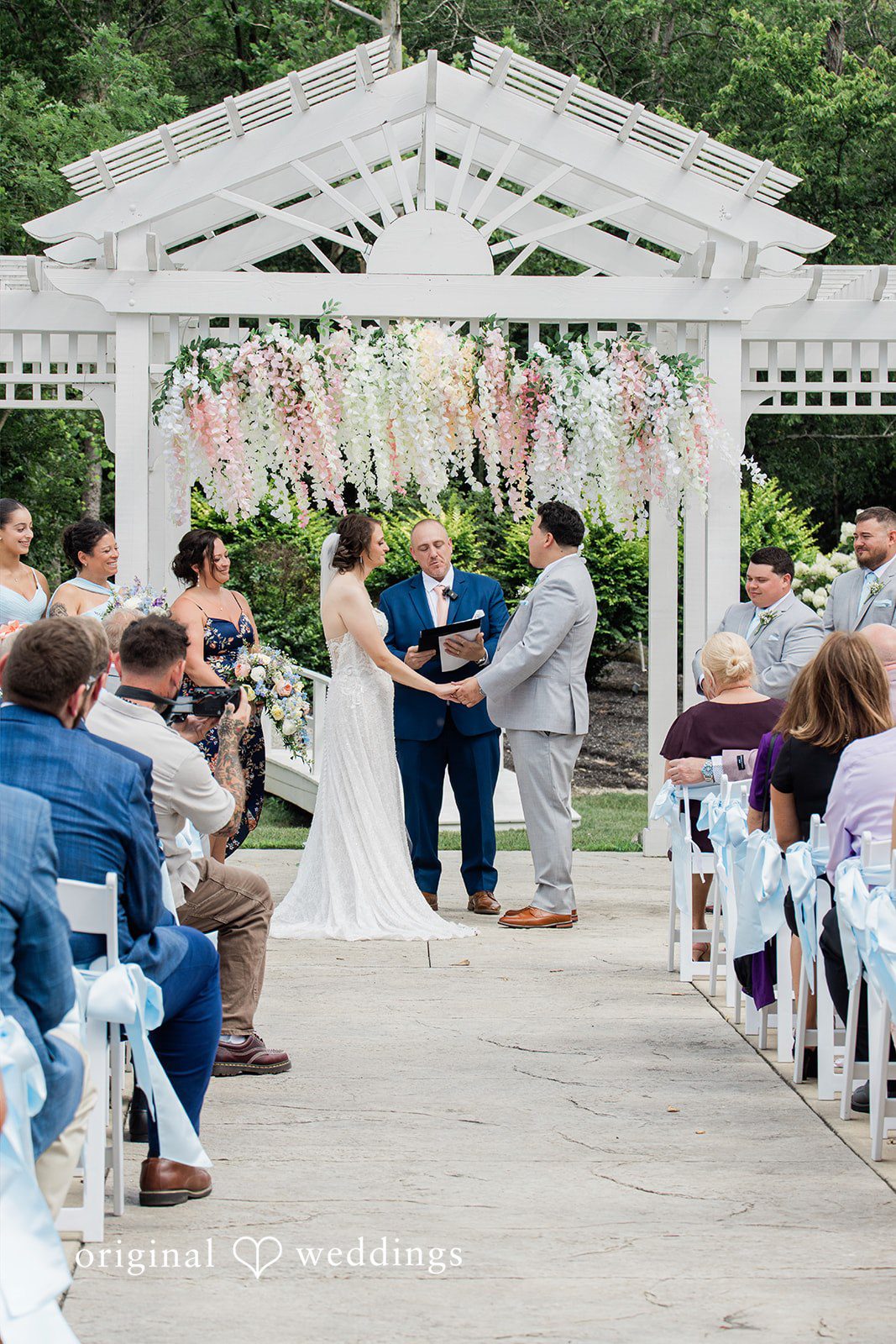 Alexander + Annalisse A wide view captures the wedding ceremony in progress beneath a white arbor structure.