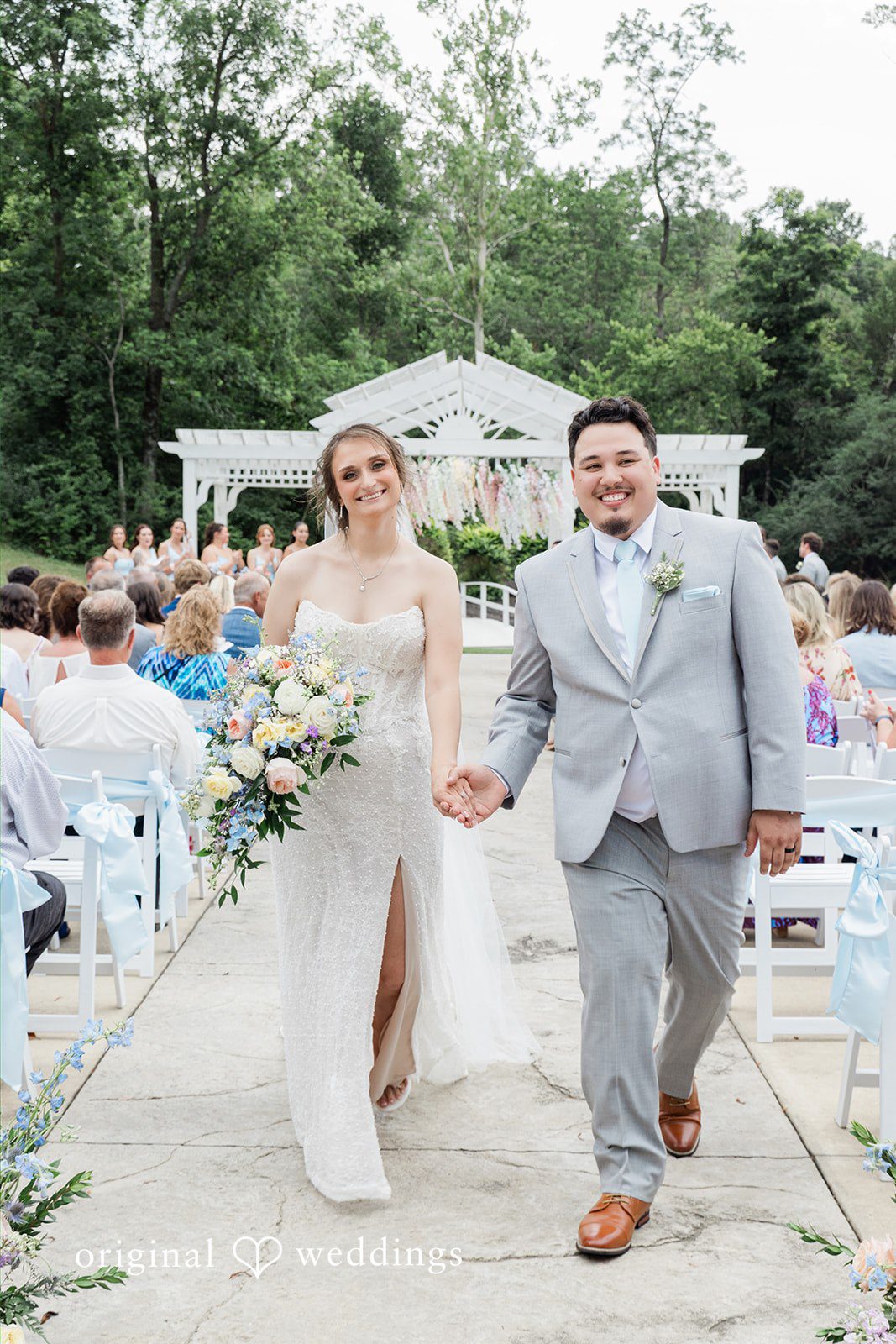 Alexander + Annalisse The newlyweds walk hand-in-hand down the aisle as guests look on.