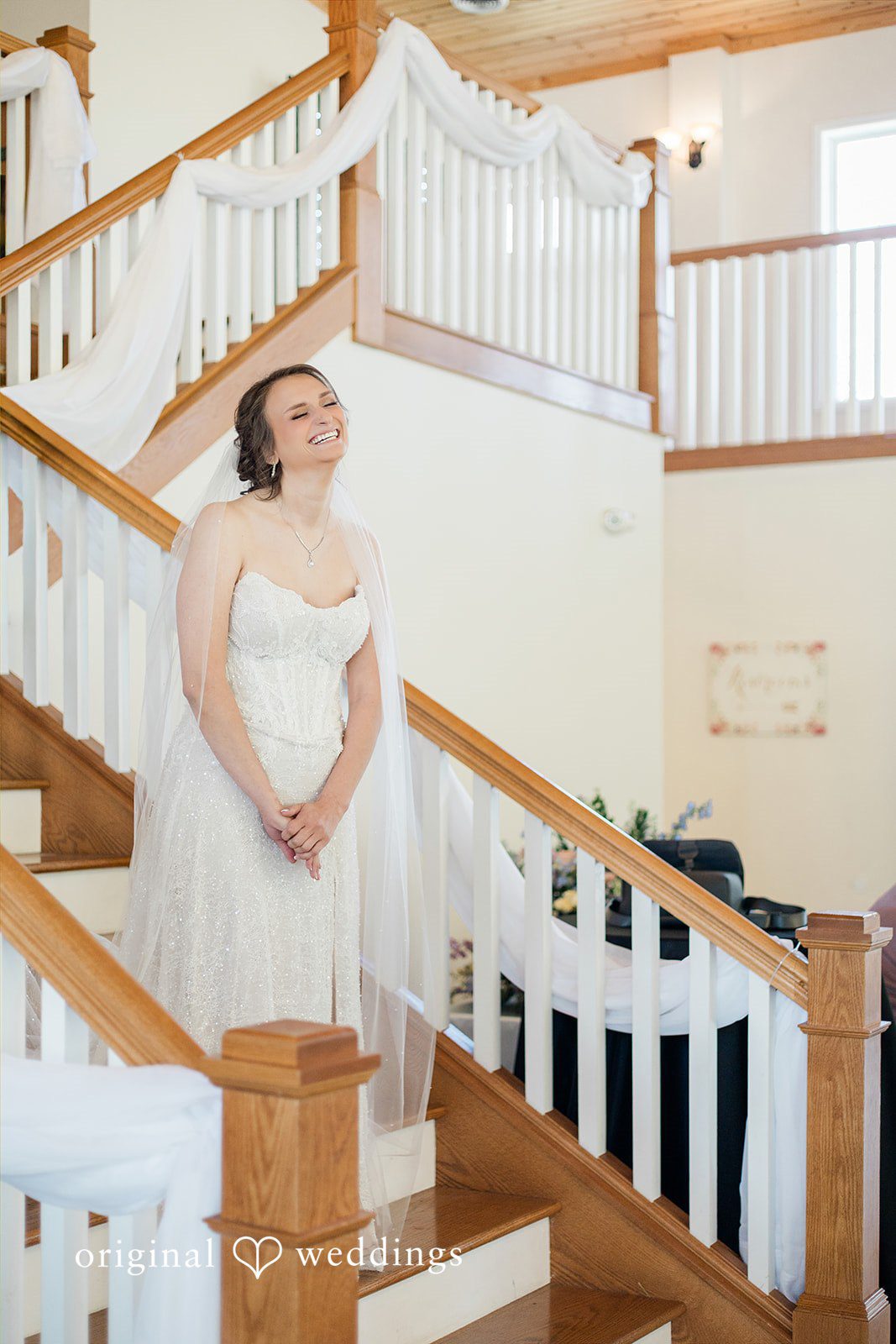Alexander + Annalisse A bride in a white gown pauses on a grand staircase with a wooden banister.